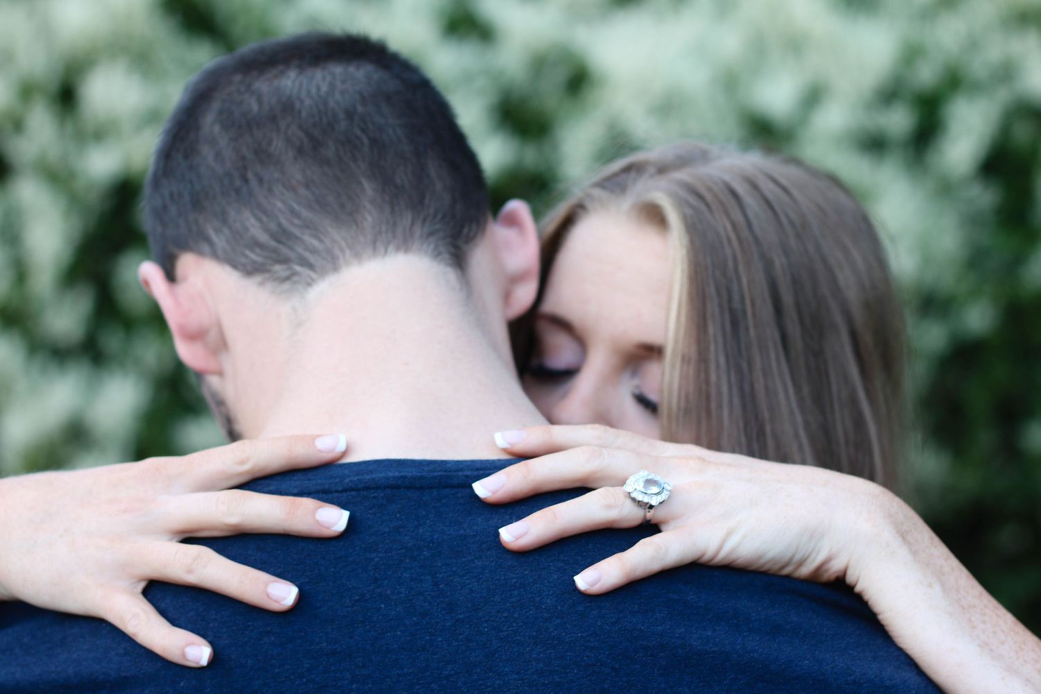 An intimate embrace captured from behind showing hands wrapped around shoulders.
