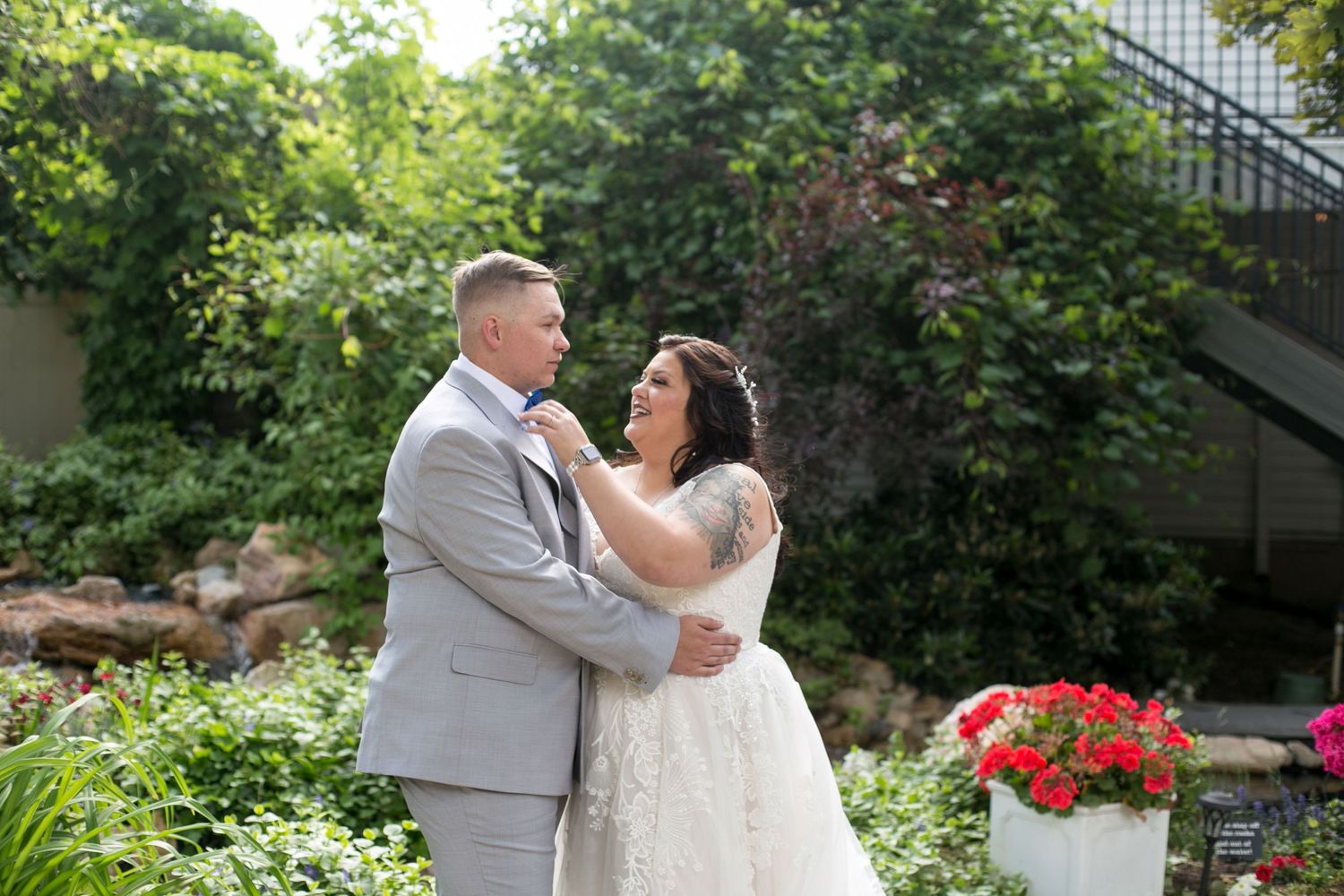 Wedding couple embraces in garden setting with red flowers and greenery.