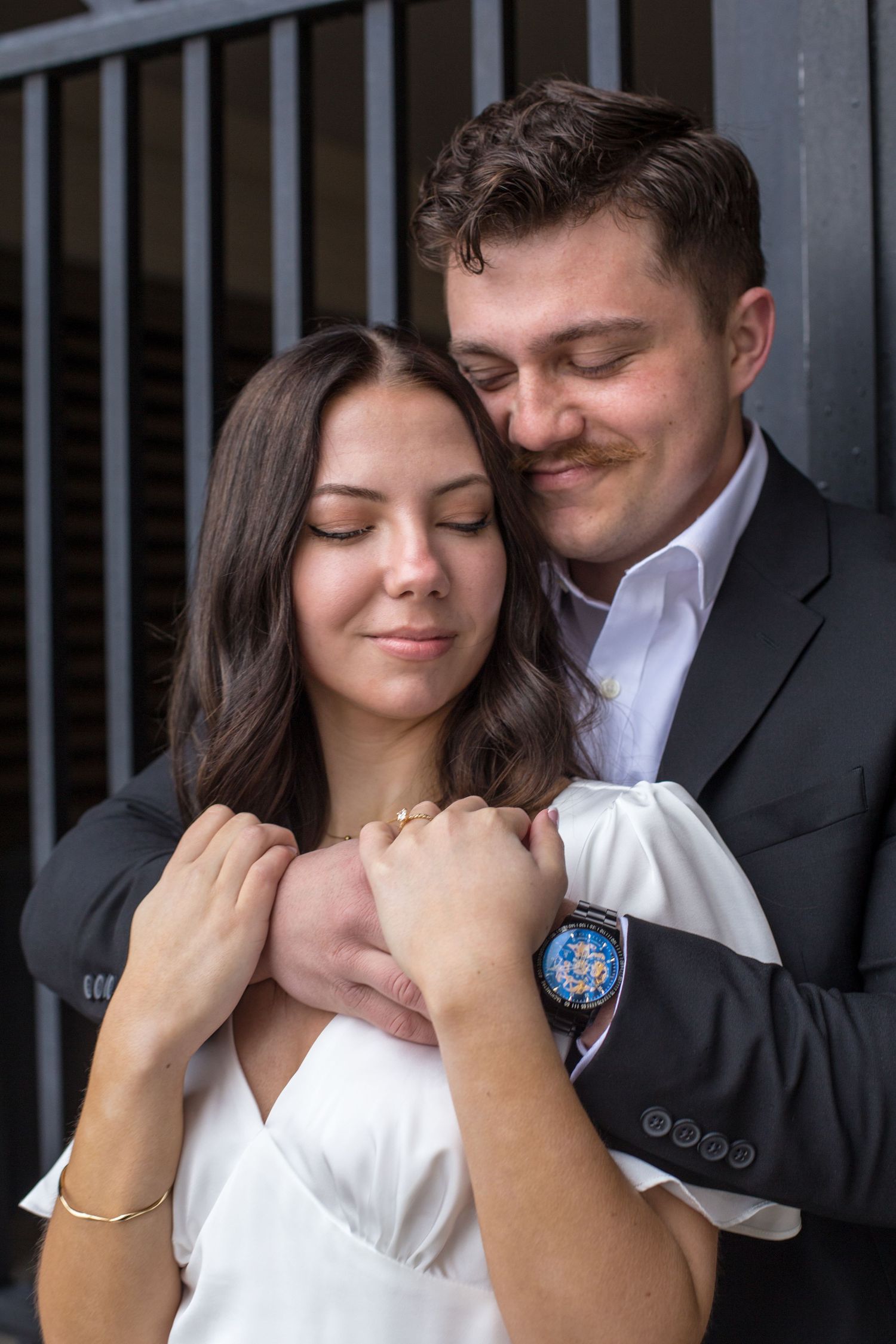 Intimate portrait of couple embracing against industrial backdrop.
