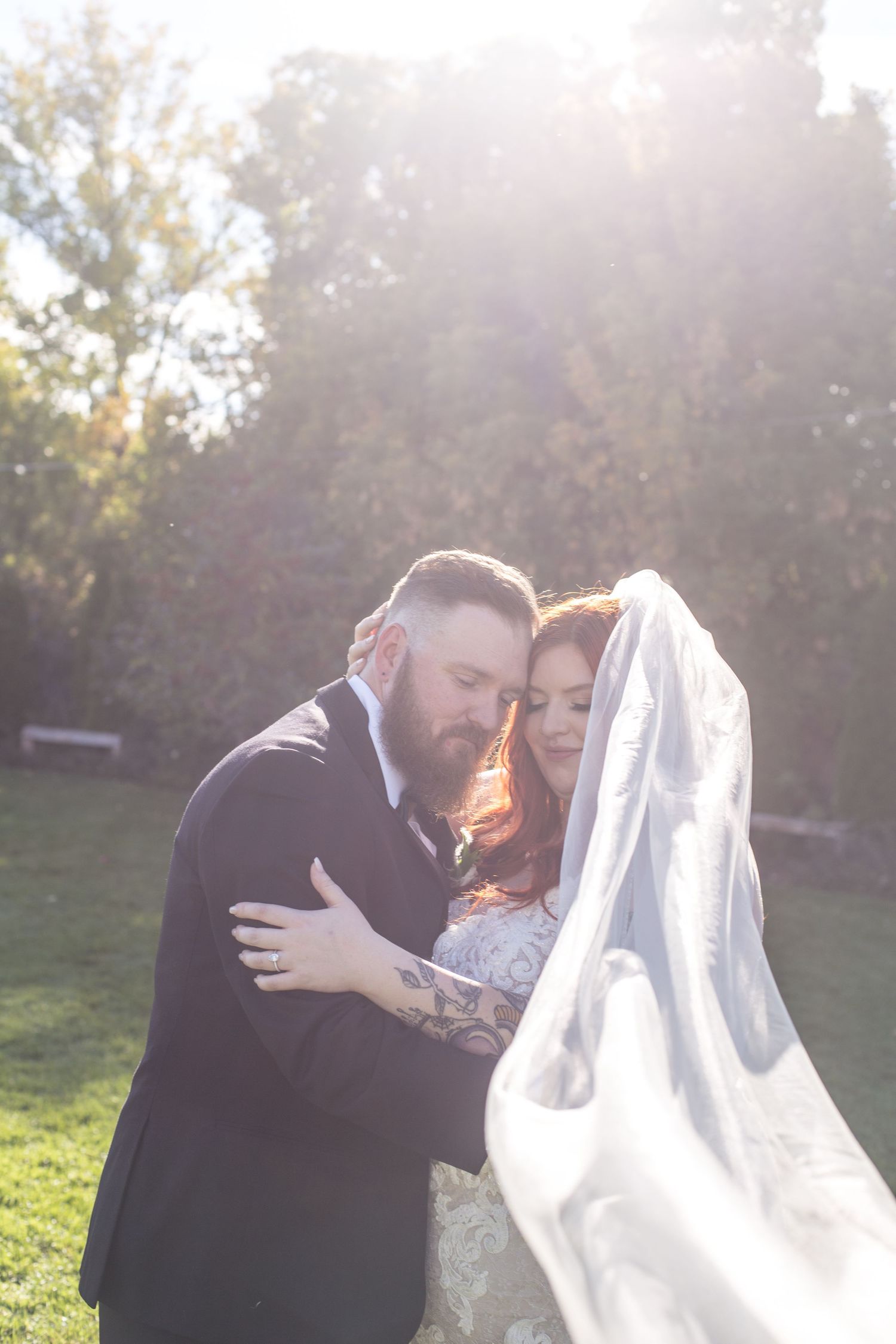 Romantic wedding couple embracing in golden sunset light with flowing veil.