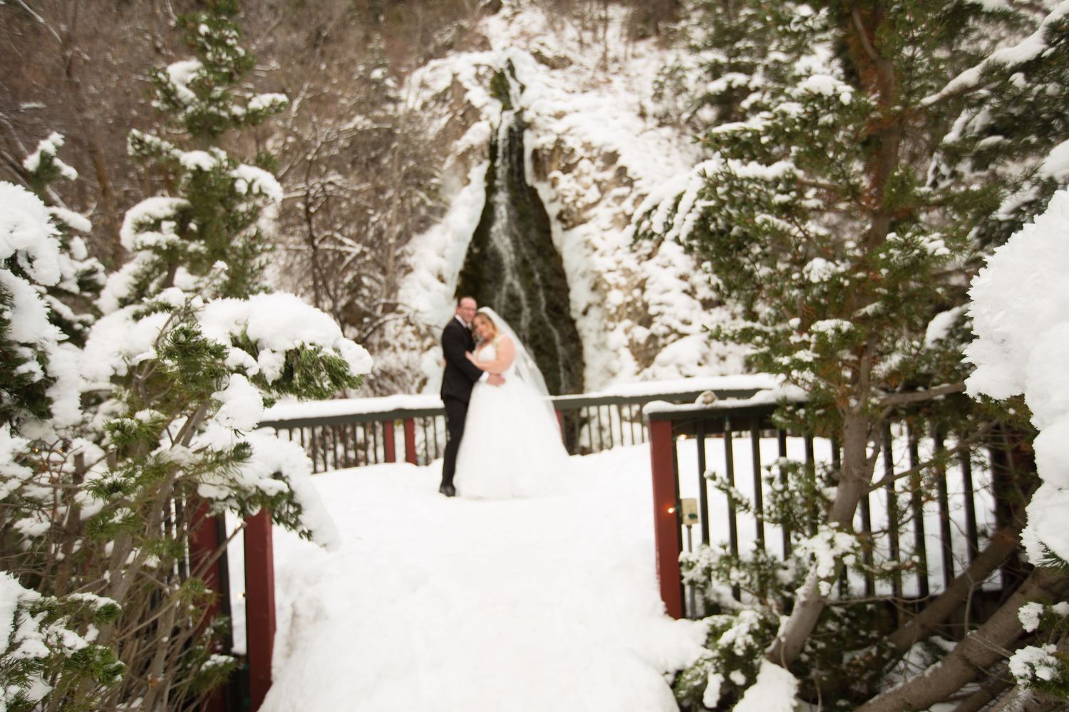 Winter wedding ceremony on snow-covered bridge with waterfall backdrop.