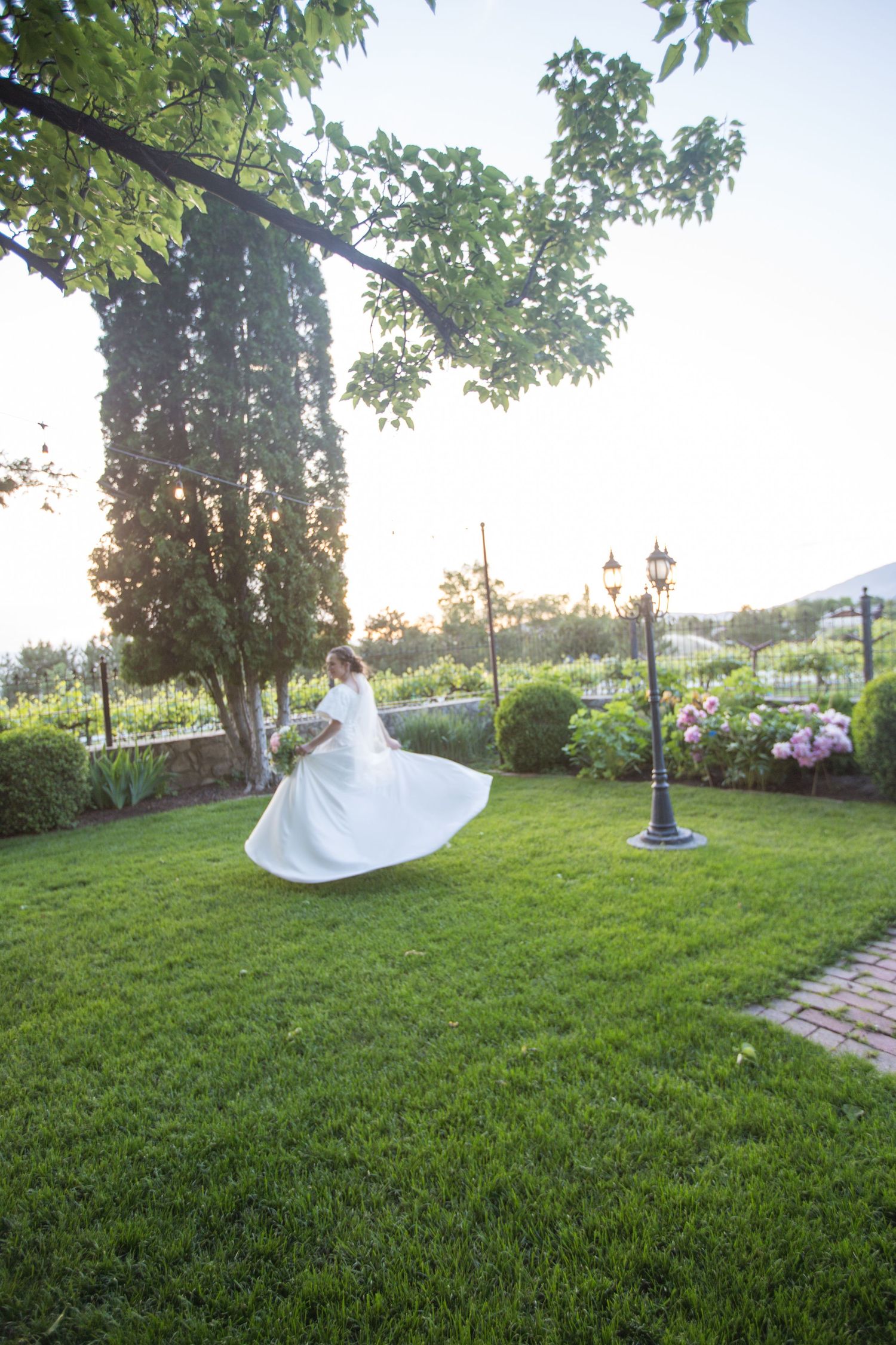 A white wedding dress spins gracefully on a manicured lawn with trees in the background.