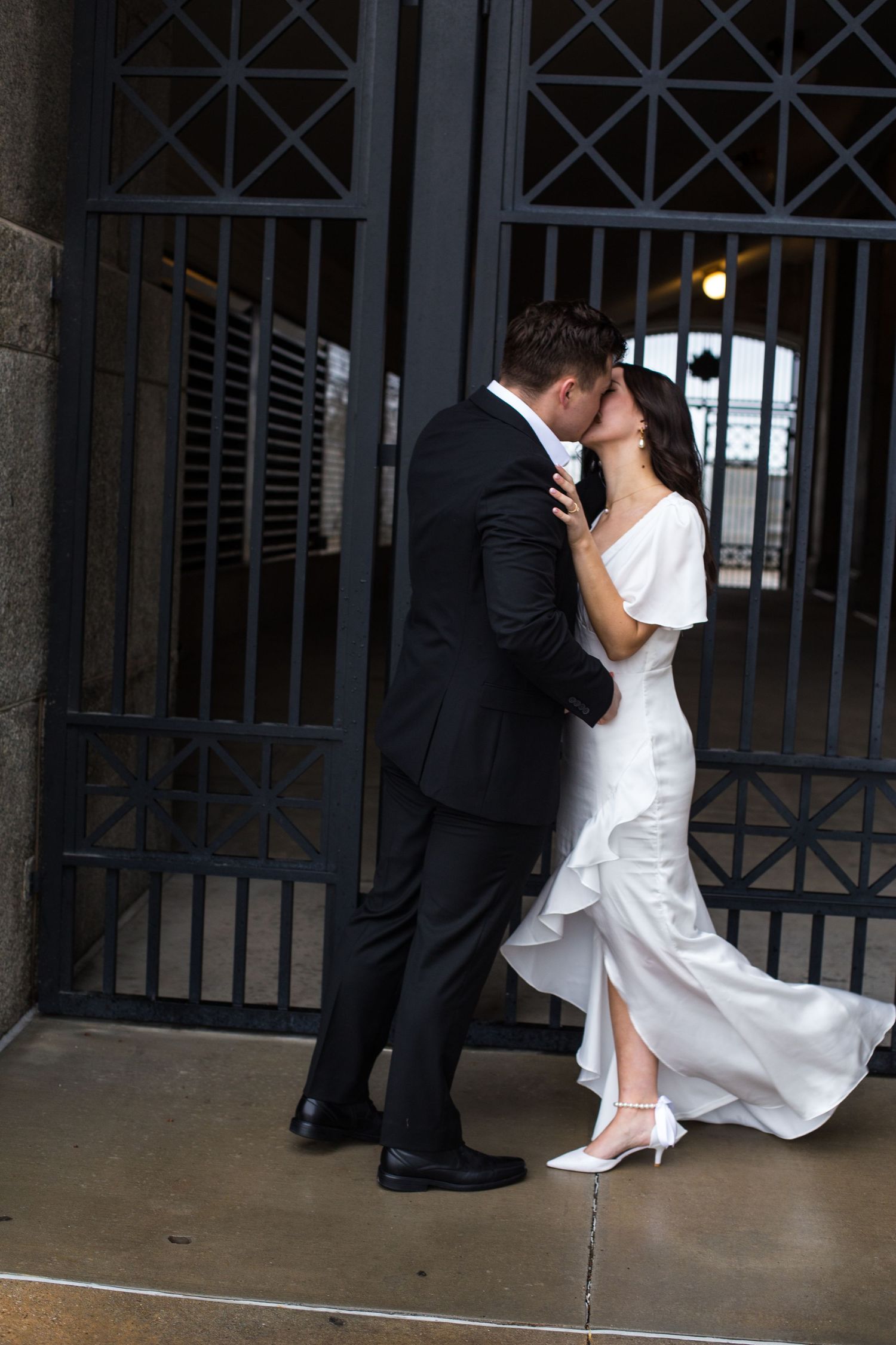 Newlyweds share an intimate moment against dark metal gates.