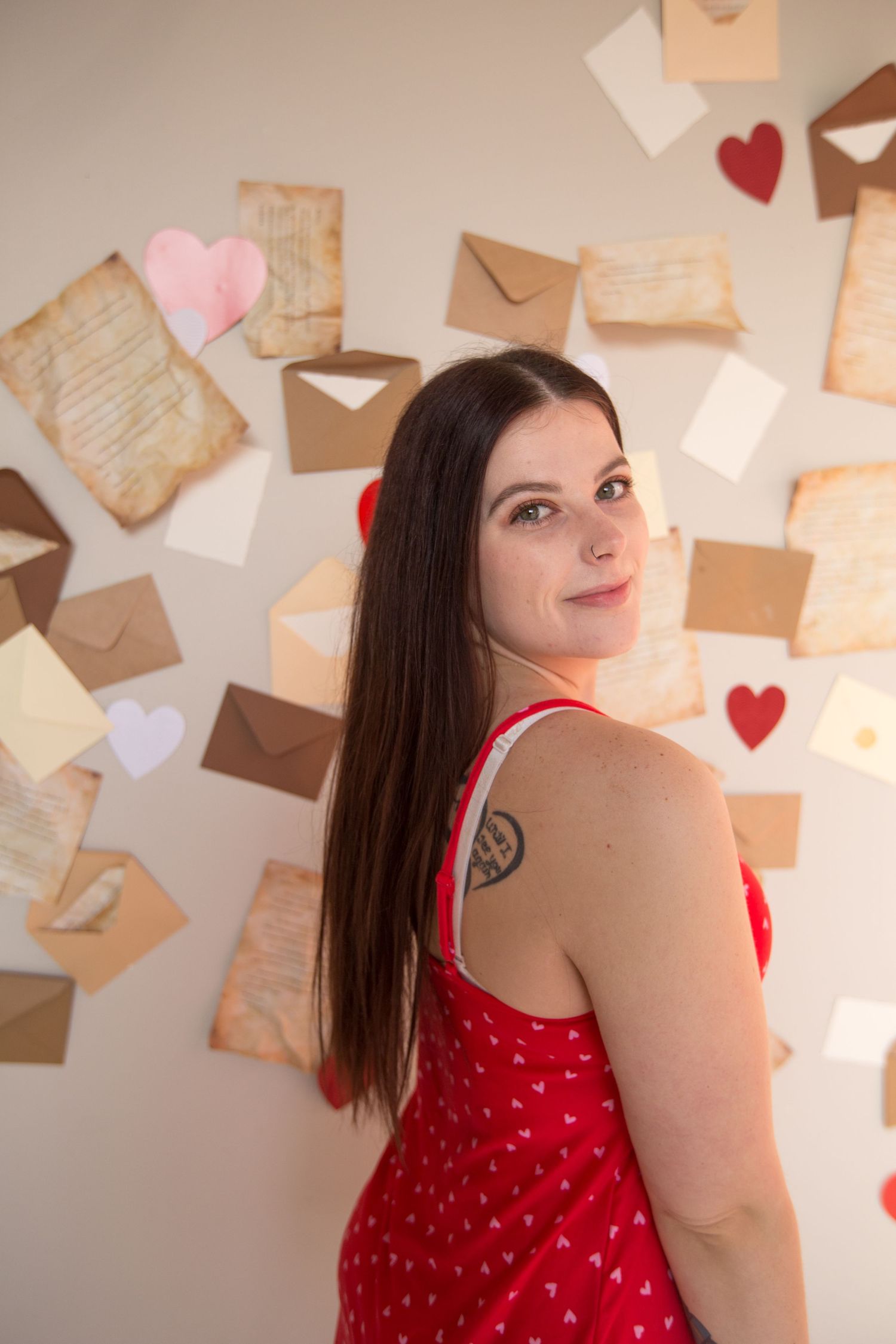 Woman in red dress poses against wall decorated with vintage letters and paper hearts.