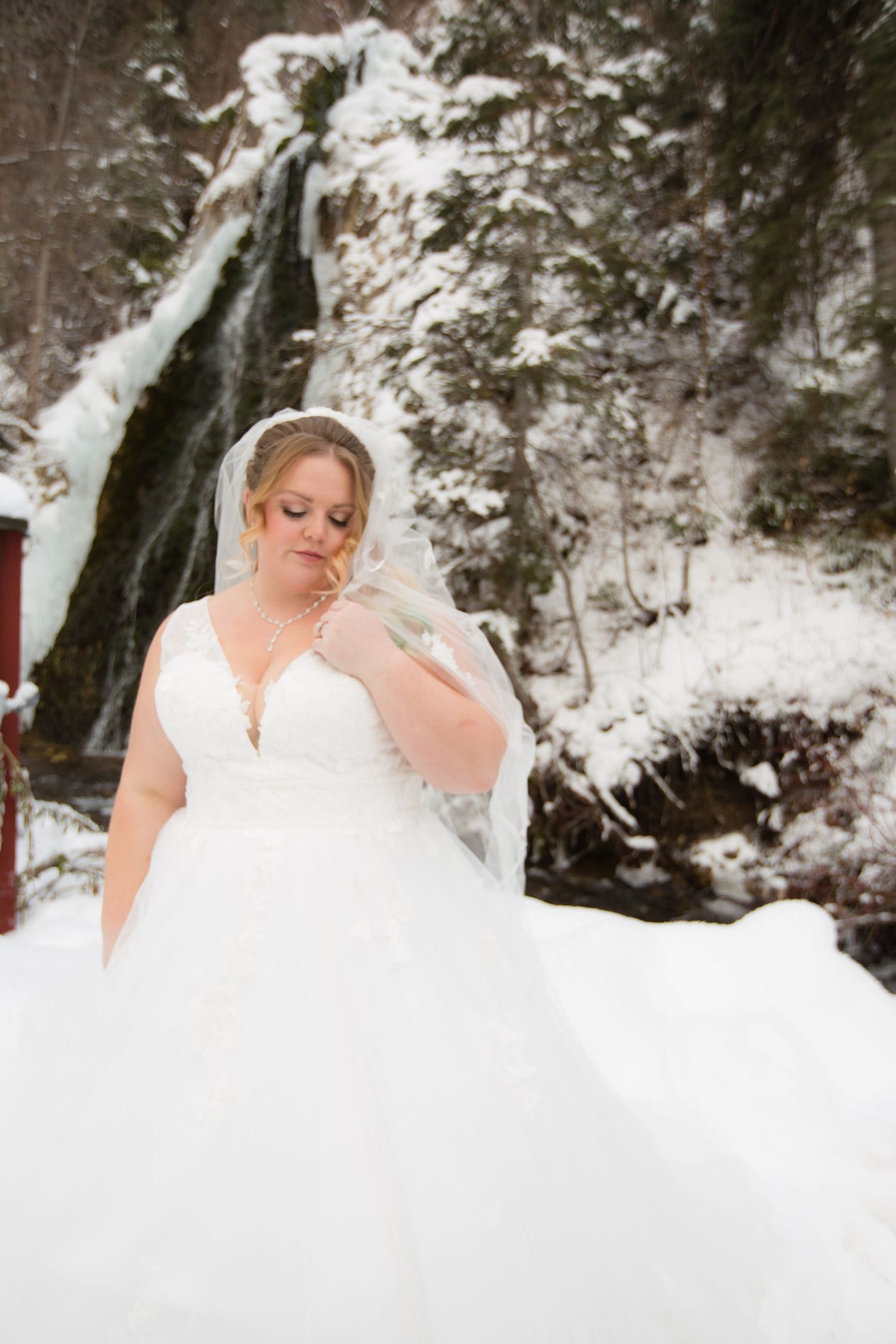 Bride in flowing white gown poses near a snow-covered waterfall.