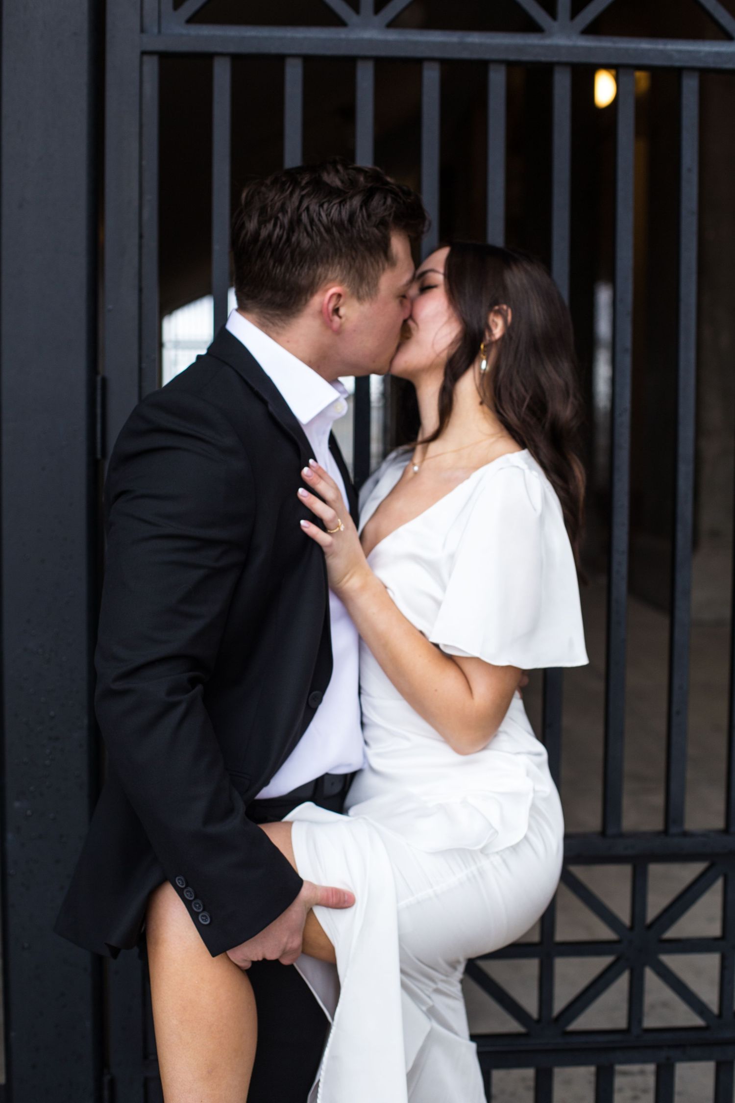 Couple shares tender moments against dark iron gates and architectural details.