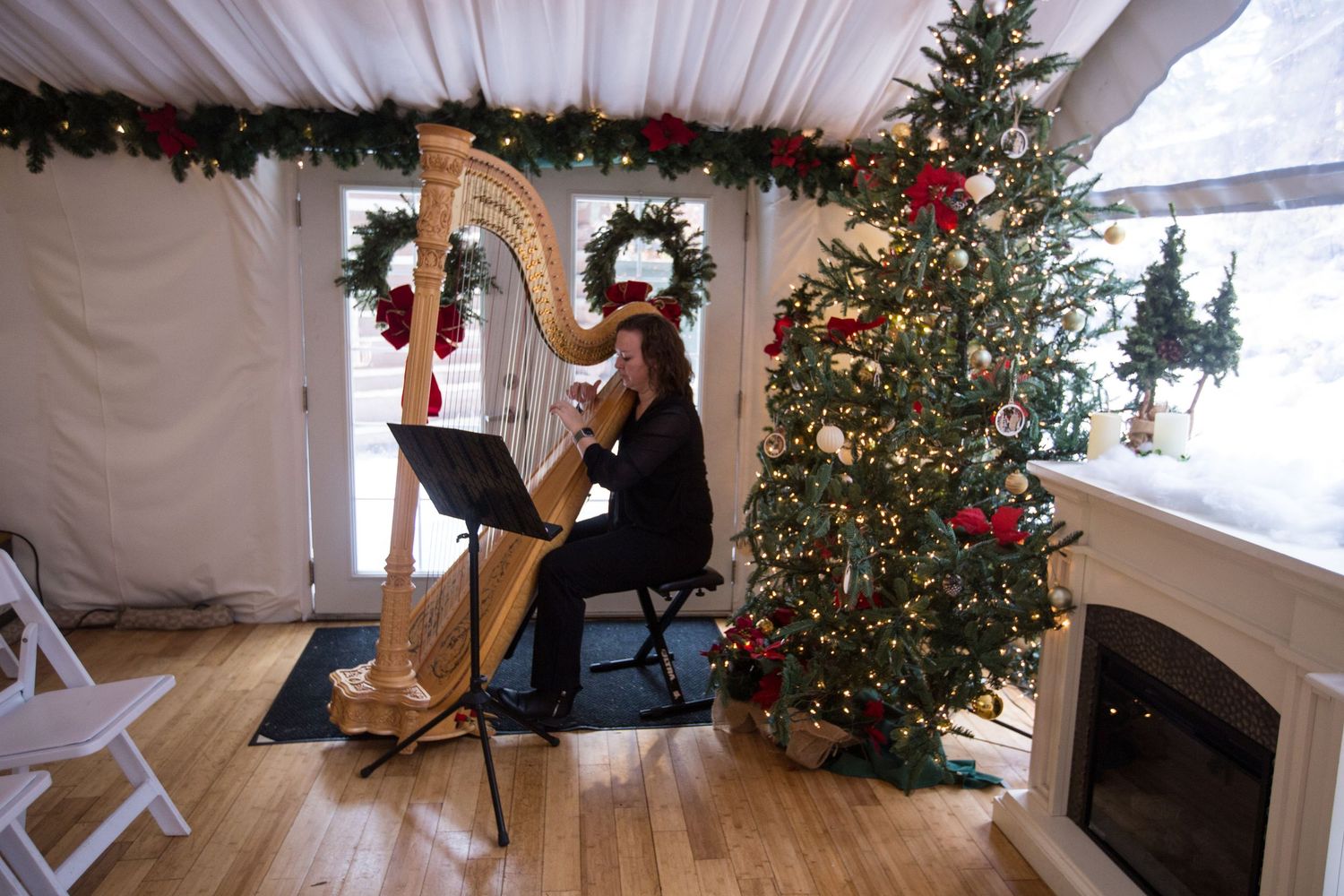 Harpist performing in a festively decorated tent with a Christmas tree and garland during a holiday event.