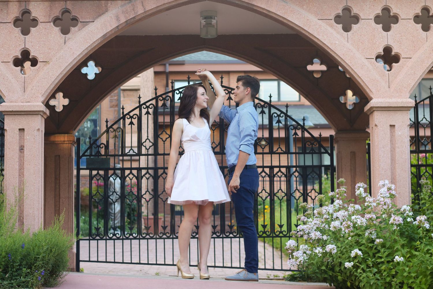 A couple poses under ornate stone archways with decorative ironwork and garden elements.