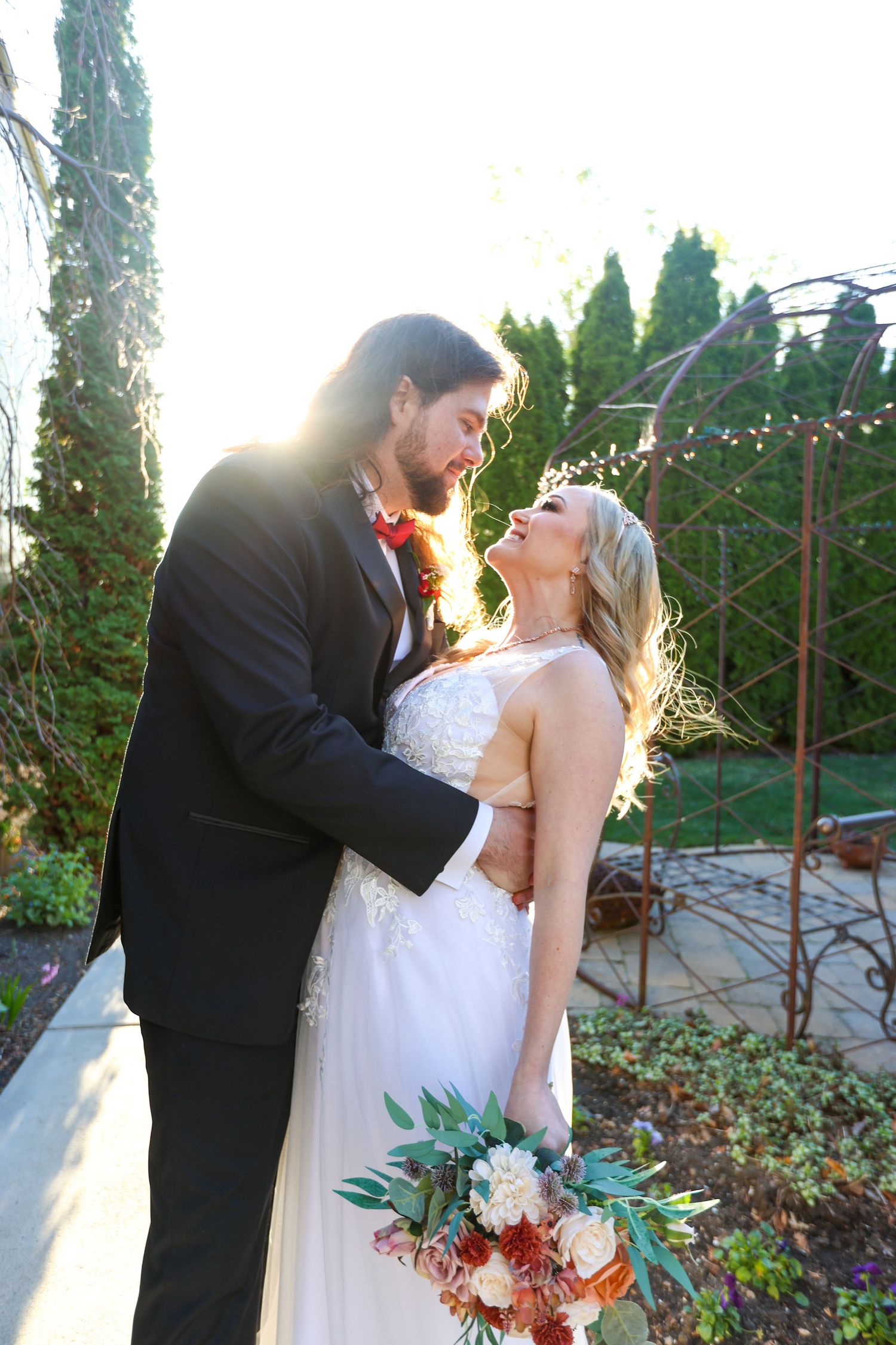 Sunset wedding portrait in a garden with sunlight creating a romantic backlit effect.