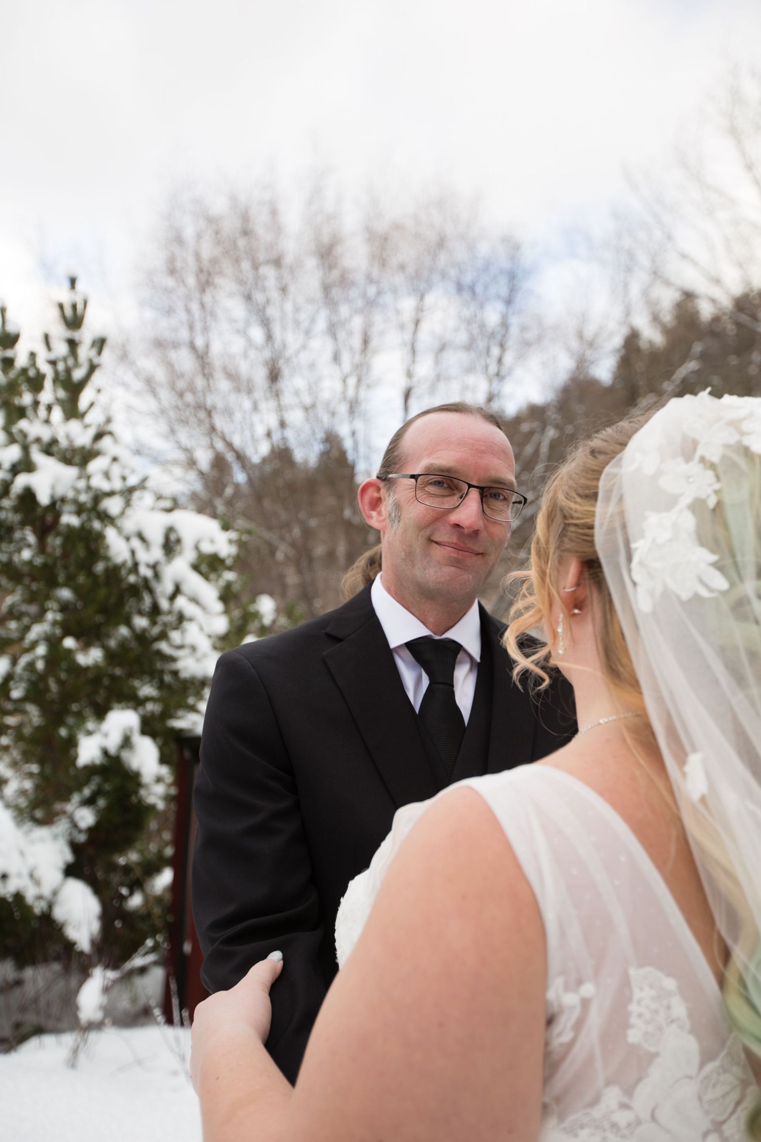 Winter wedding portrait with snow covered evergreens in the background.