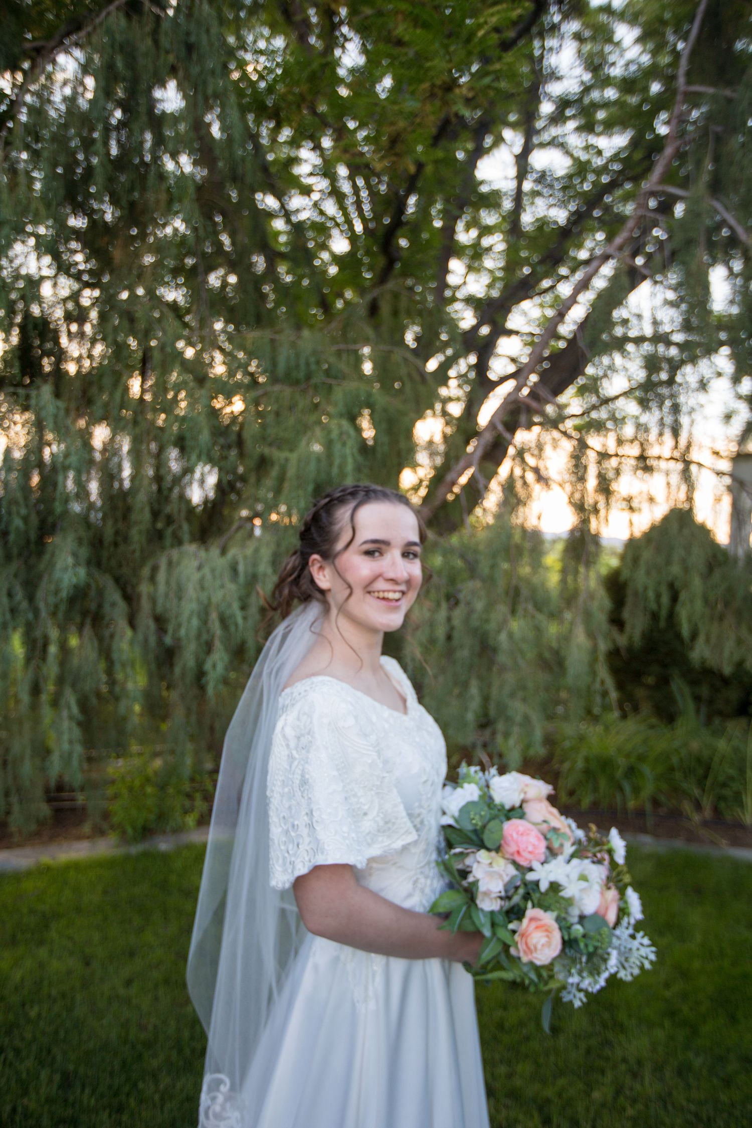 A flowing white wedding dress with floral bouquet photographed in an outdoor garden setting.
