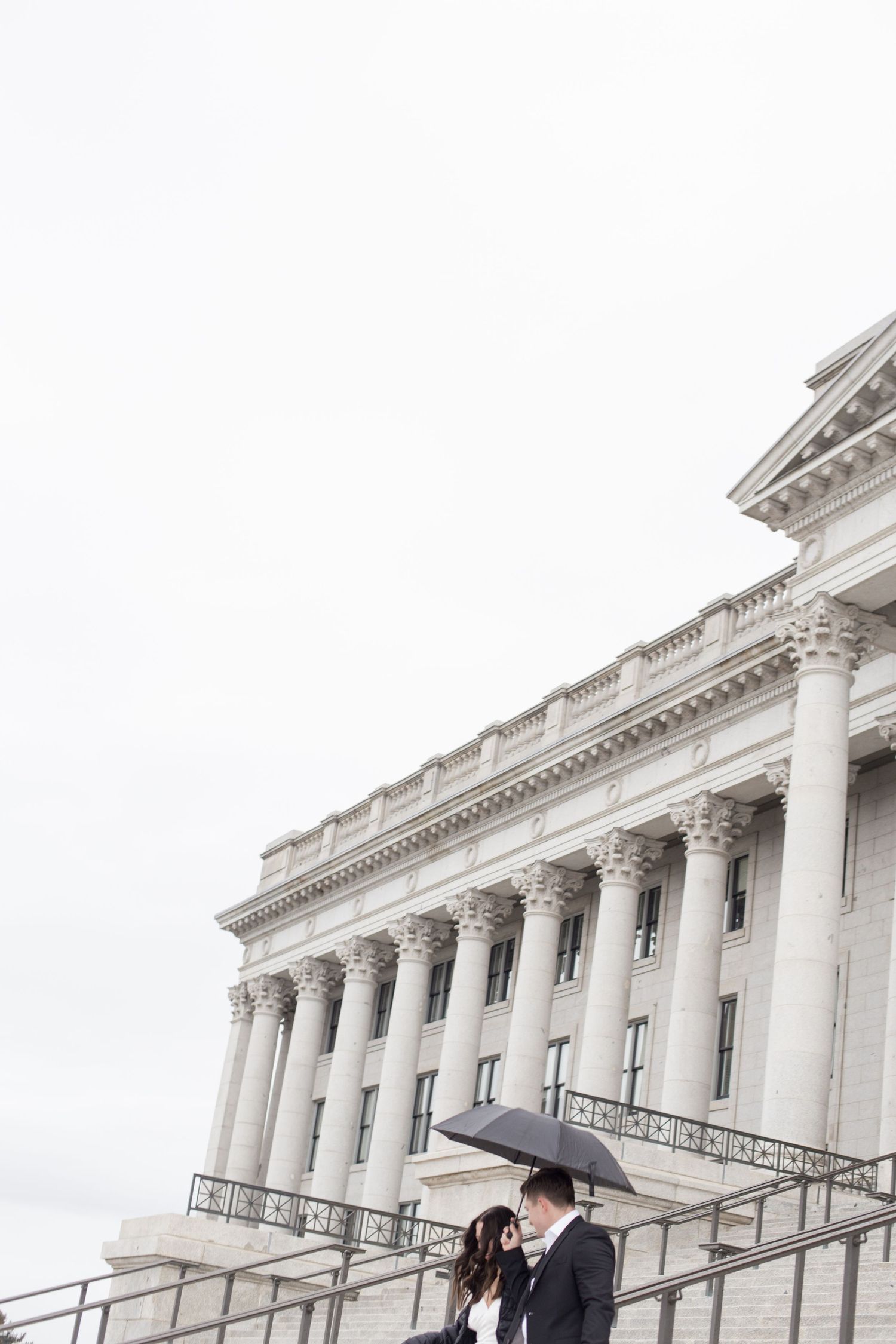 Romantic couple embraces on steps of a stately government building with white columns.