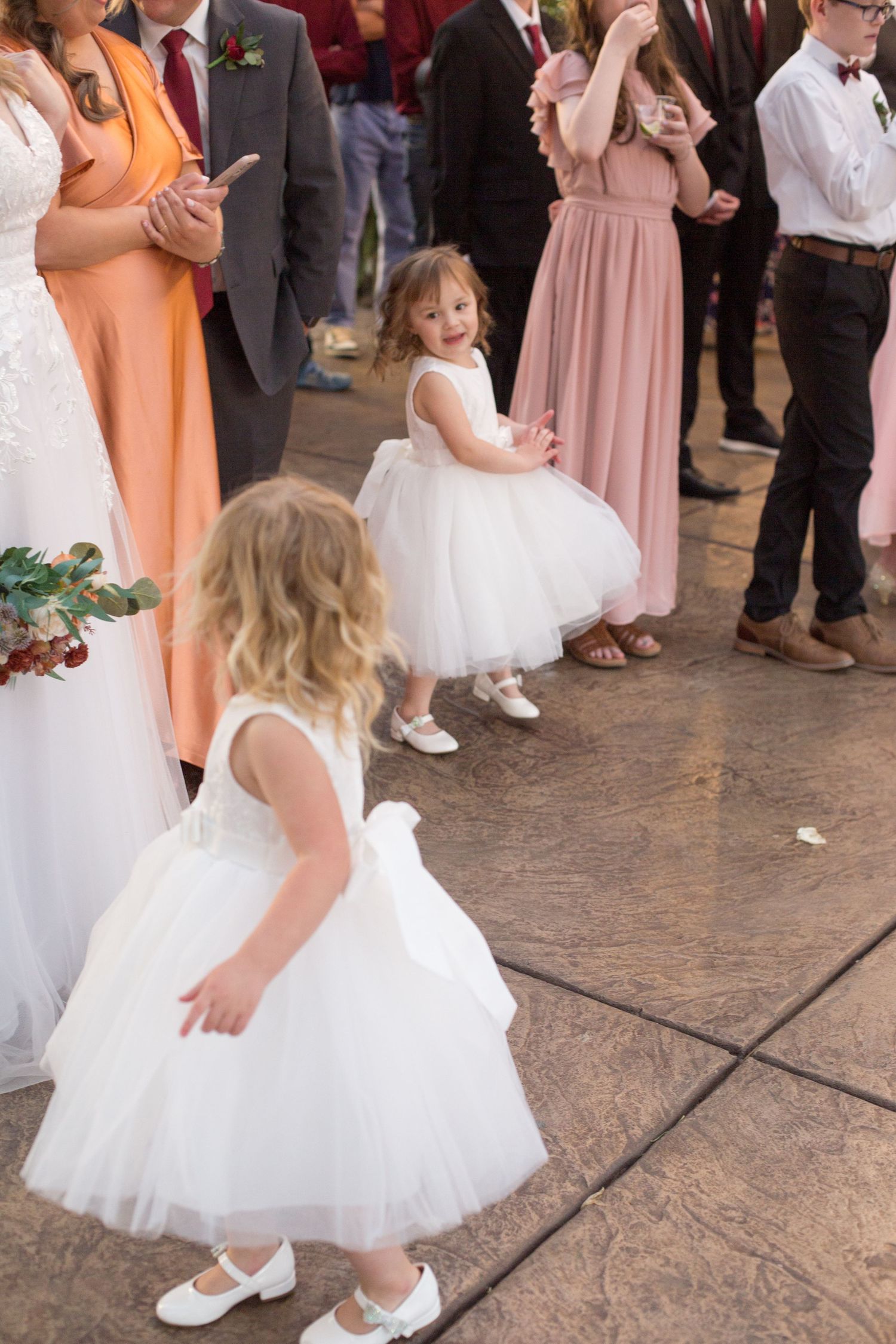 Young girls in white dresses and flats dance together at a wedding reception.