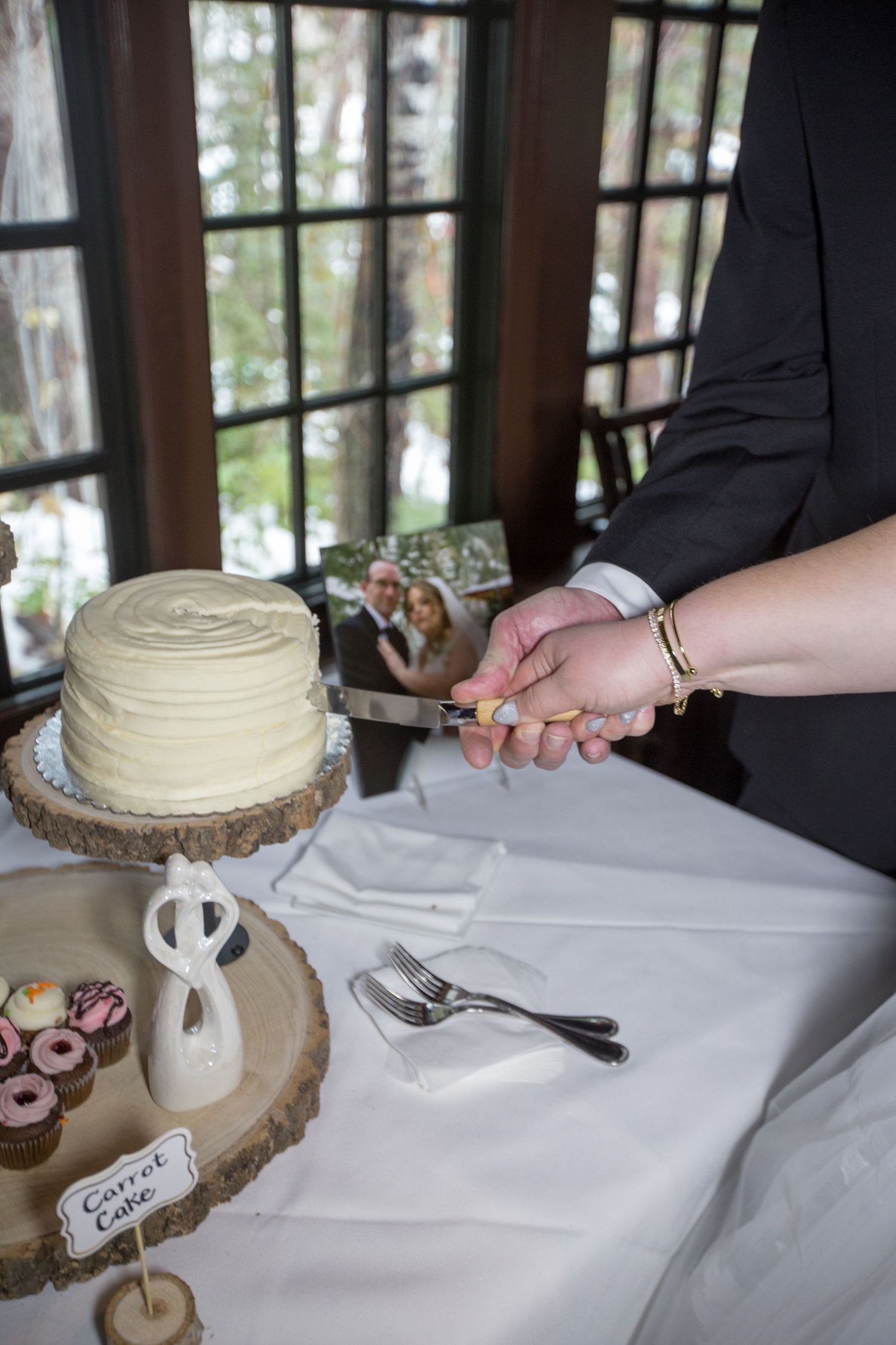 Bride and groom cutting a white frosted wedding cake on a rustic wood stand at their elegant reception.