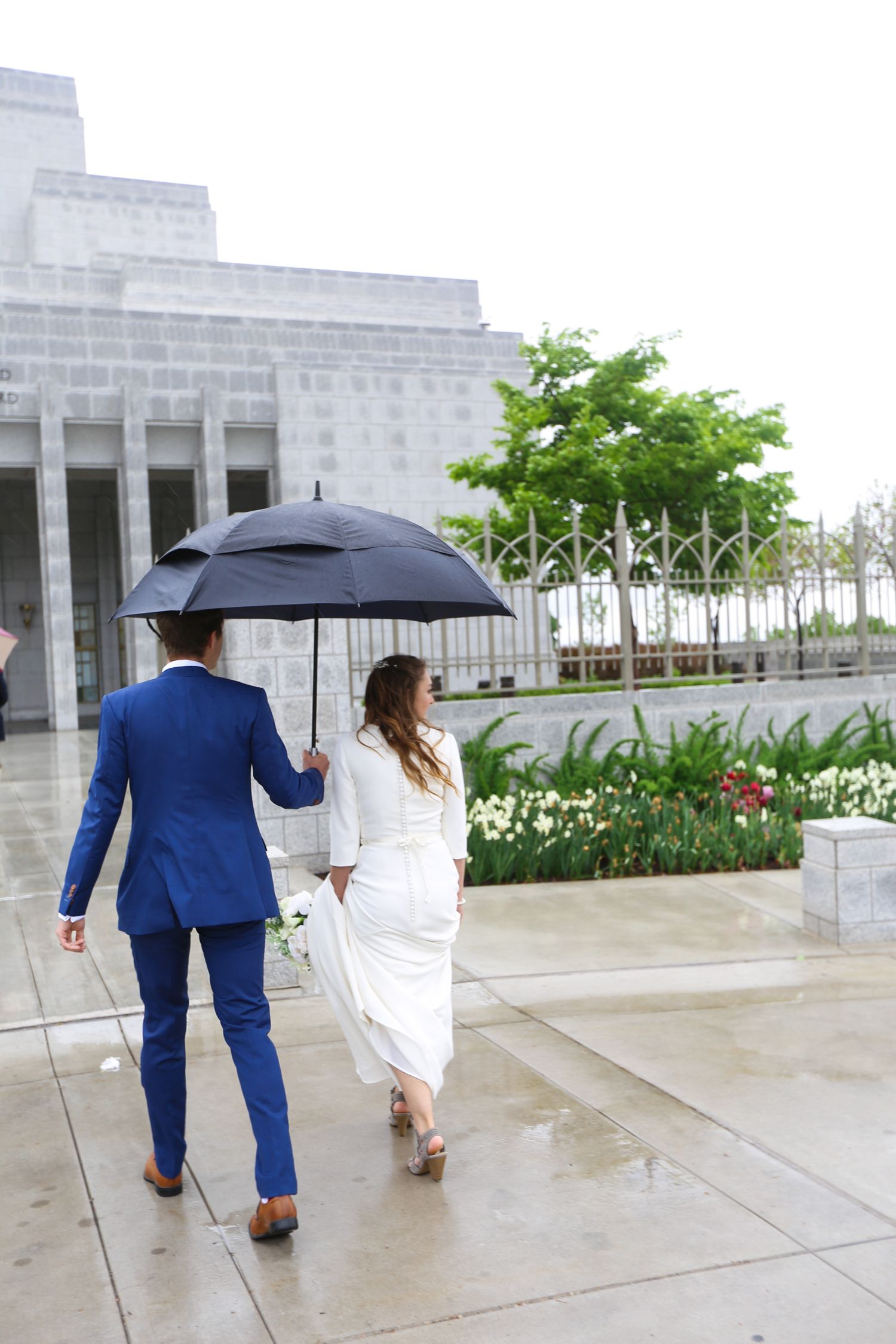 A rainy wedding day photo shoot with umbrellas outside a grand stone building.