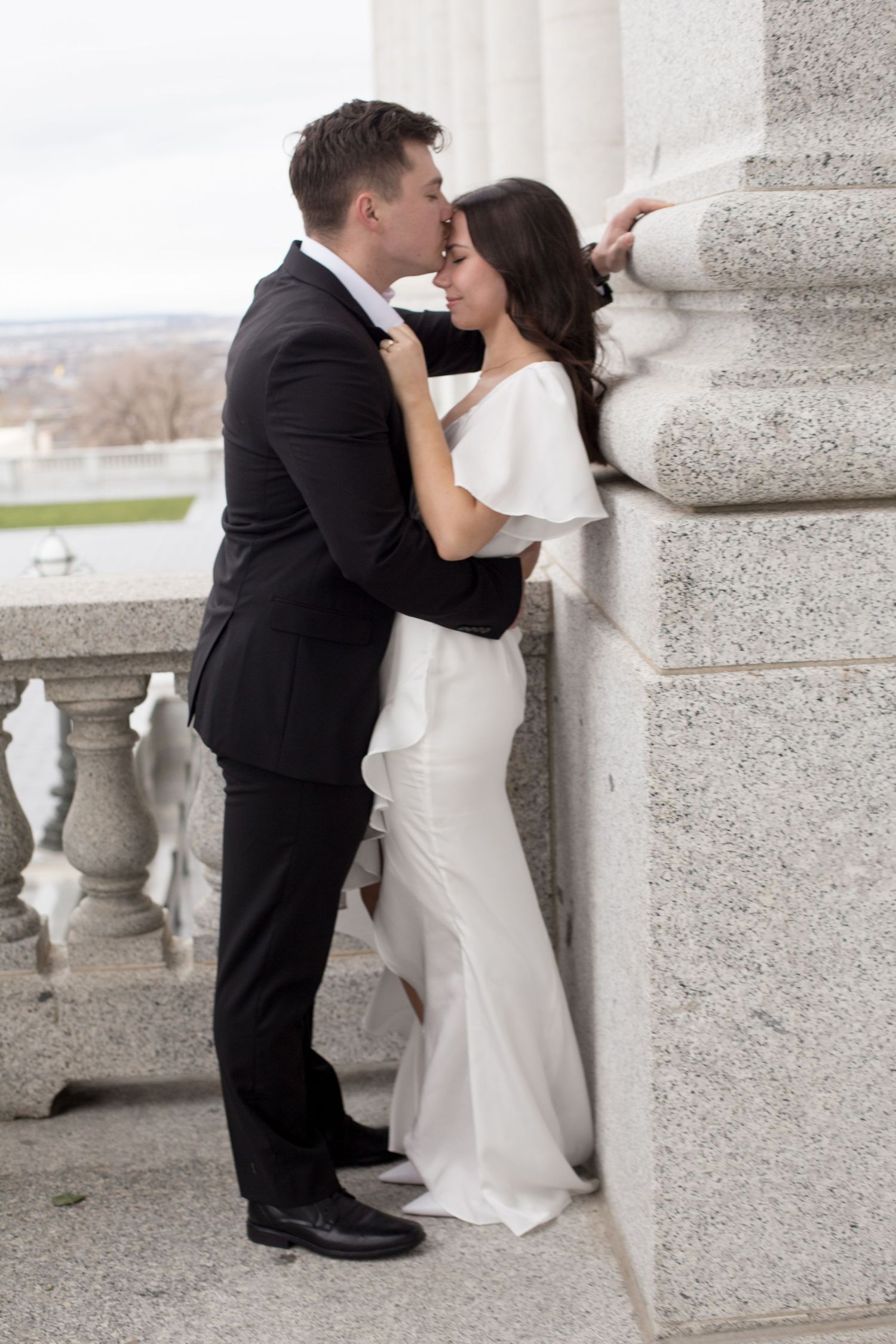 An intimate embrace between a couple in wedding attire against classical stone architecture.