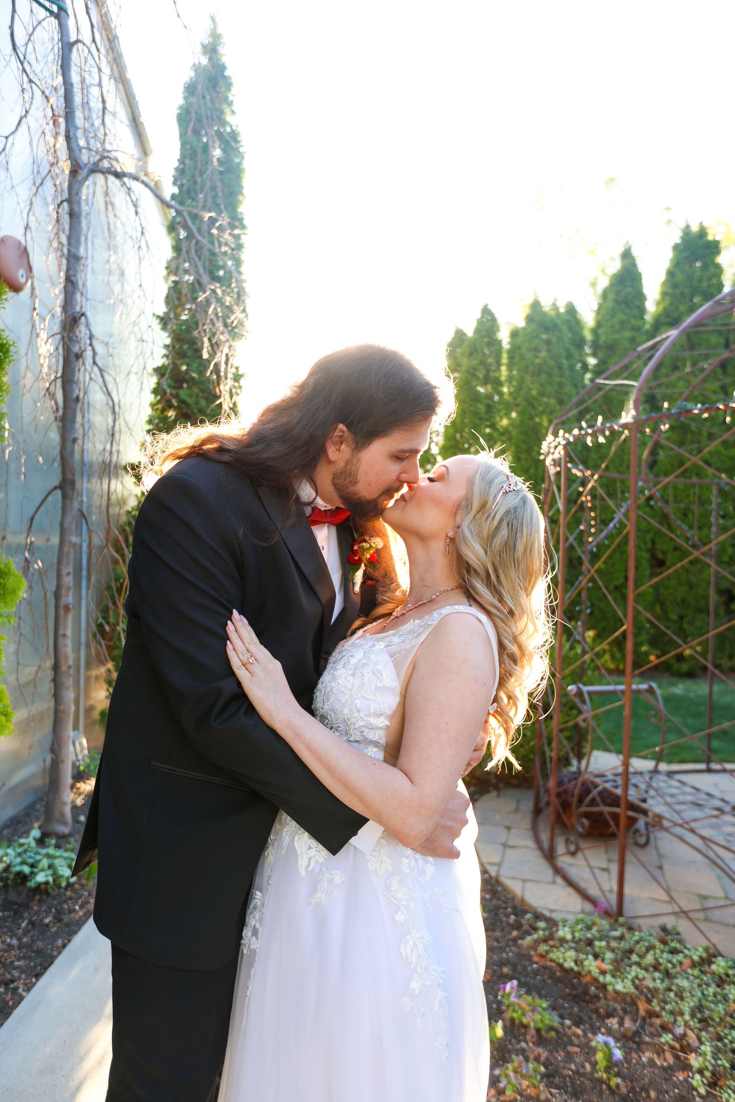 Romantic sunset wedding portraits under an ornate garden structure.