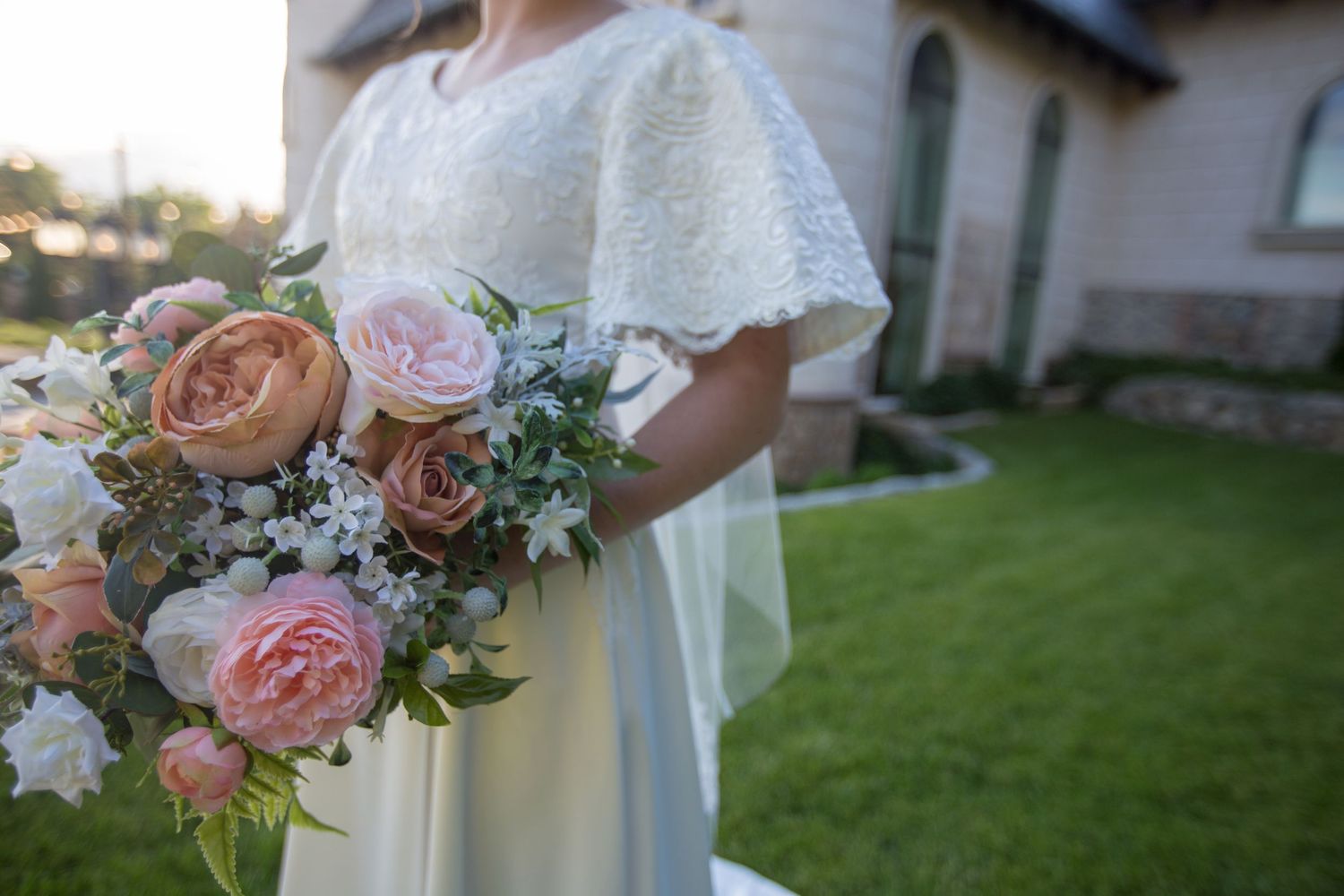 Close-up of romantic peach and pink wedding bouquet with roses against white bridal gown.