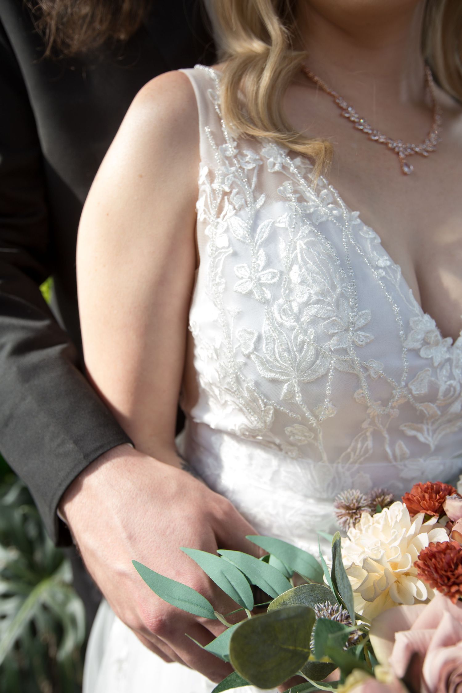 Close up detail of an elegant white lace wedding dress with floral embellishments.
