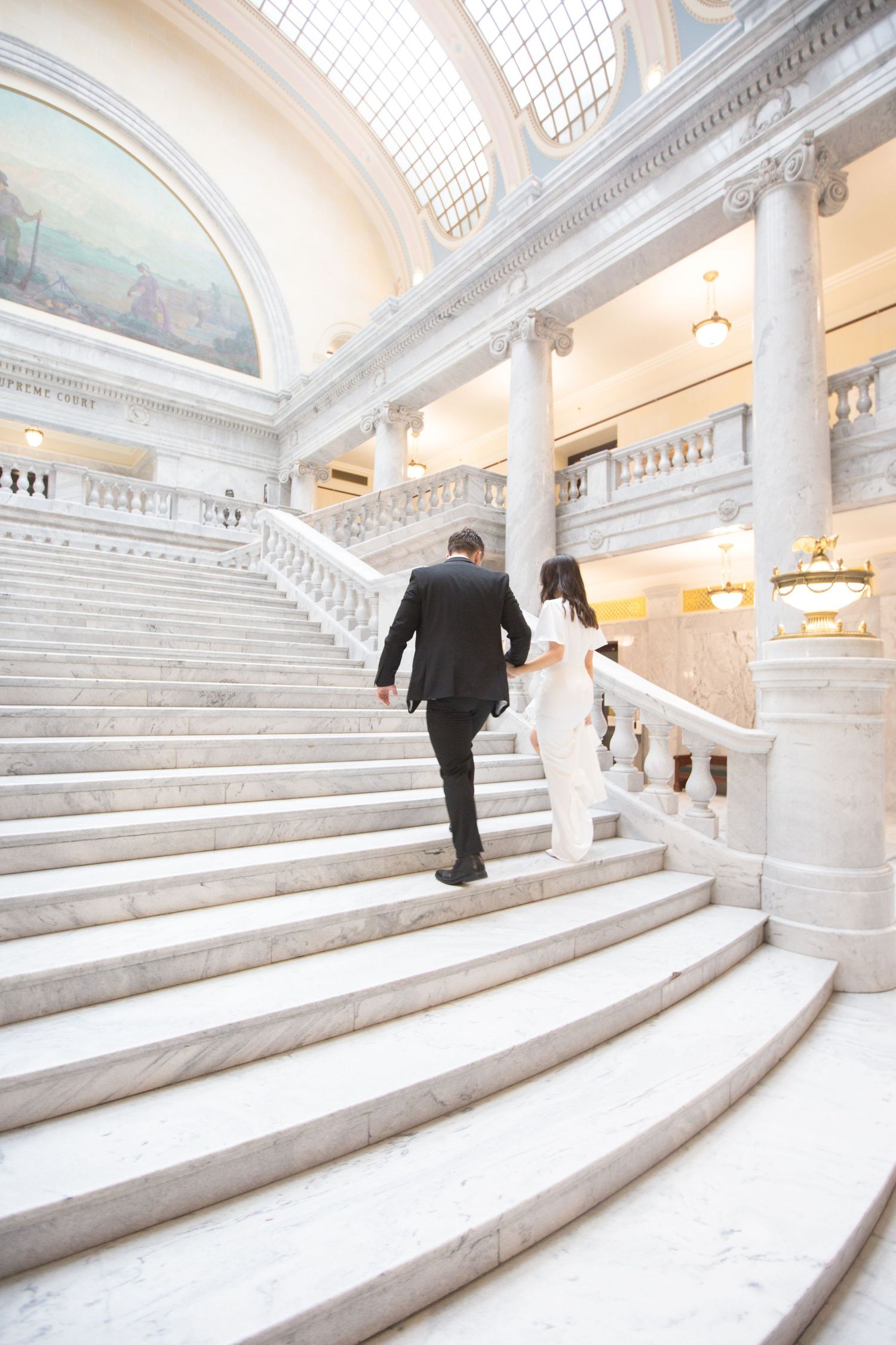 Figure ascending elegant white marble staircase in historic building interior.