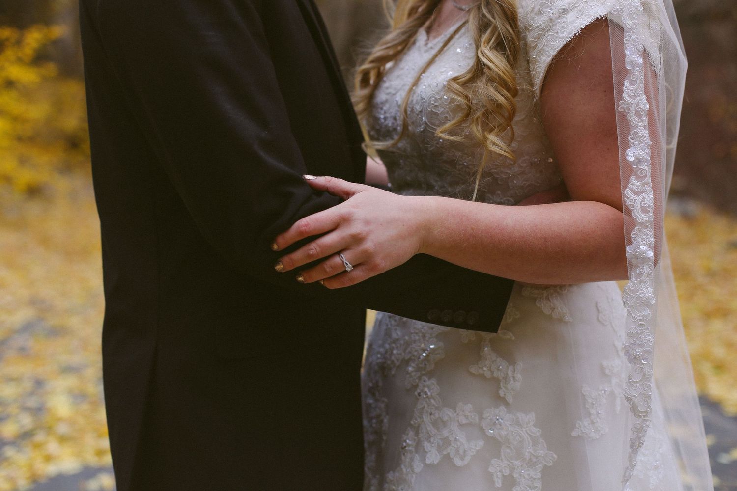Close-up details of bride and groom embracing during their autumn wedding.