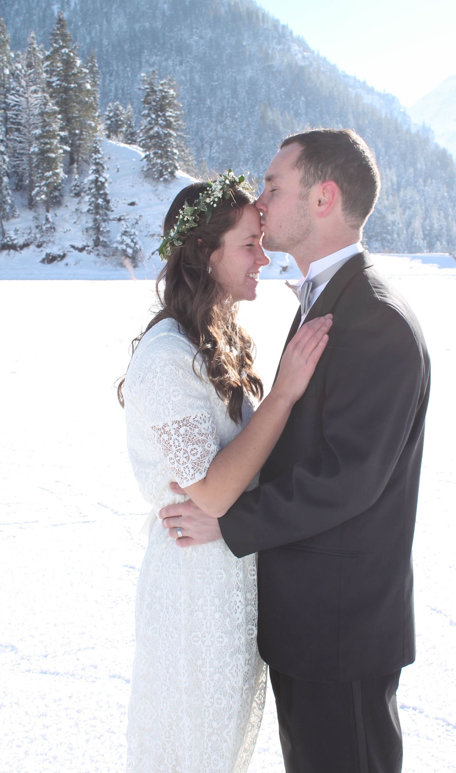 Winter wedding couple shares romantic moment against snowy mountain backdrop.