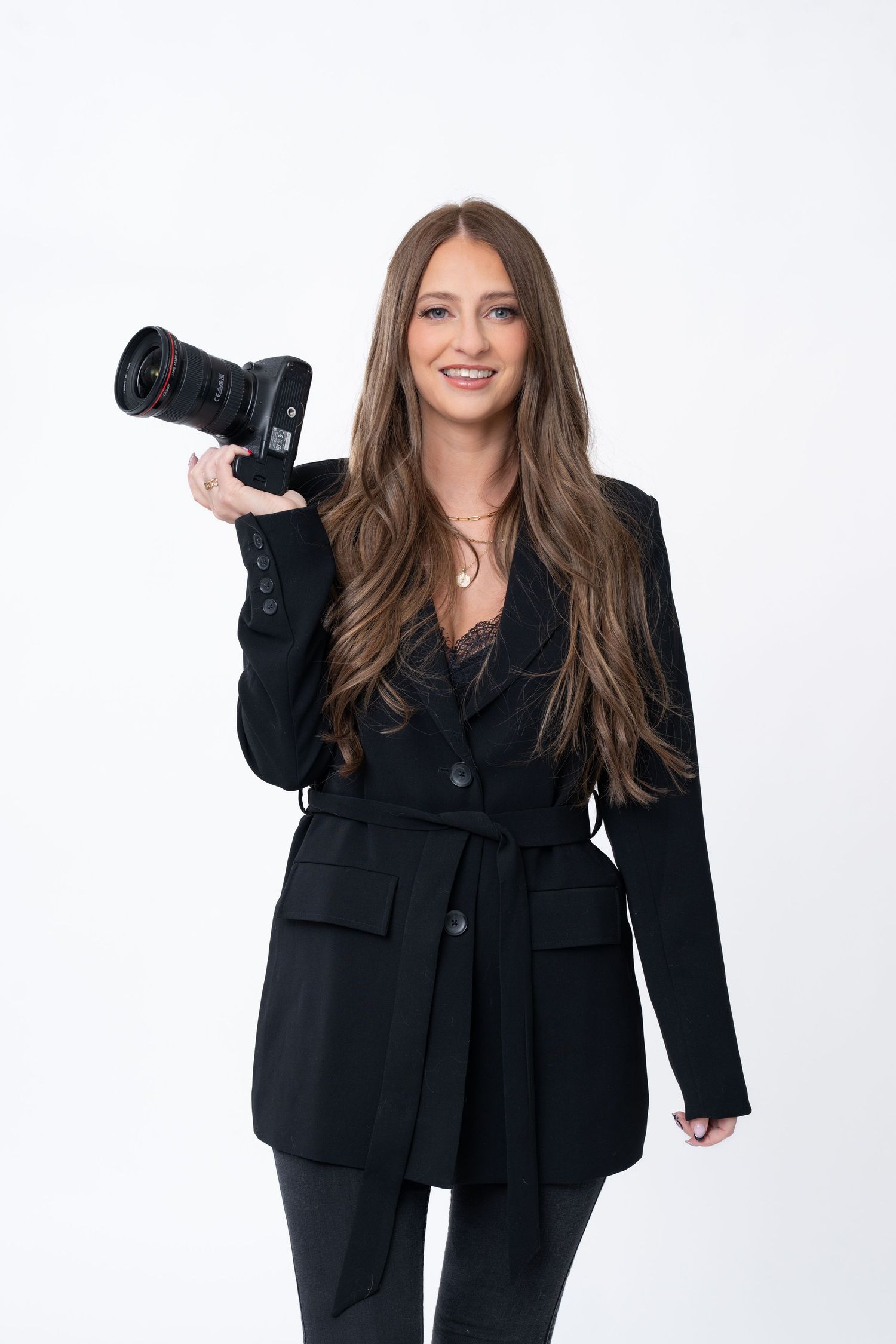 Playful studio portraits of photographer with professional camera wearing black outfit.