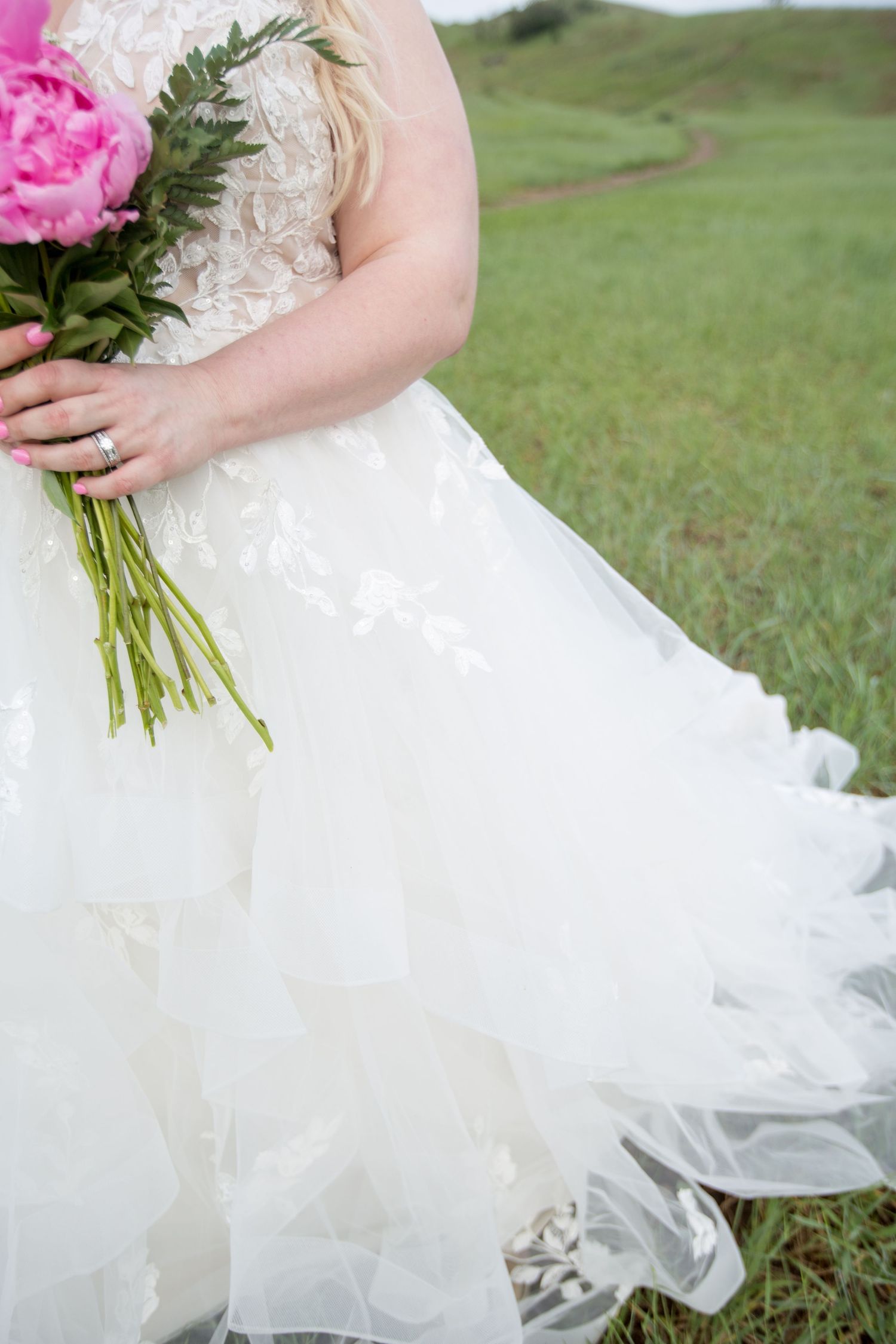 Elegant white wedding dress billows in the breeze while holding vibrant pink peonies.