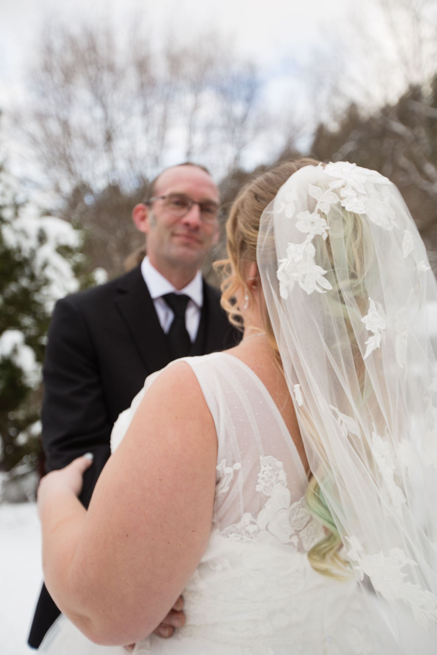 A romantic winter wedding moment captured from behind the bride wearing a flowing white dress and veil.