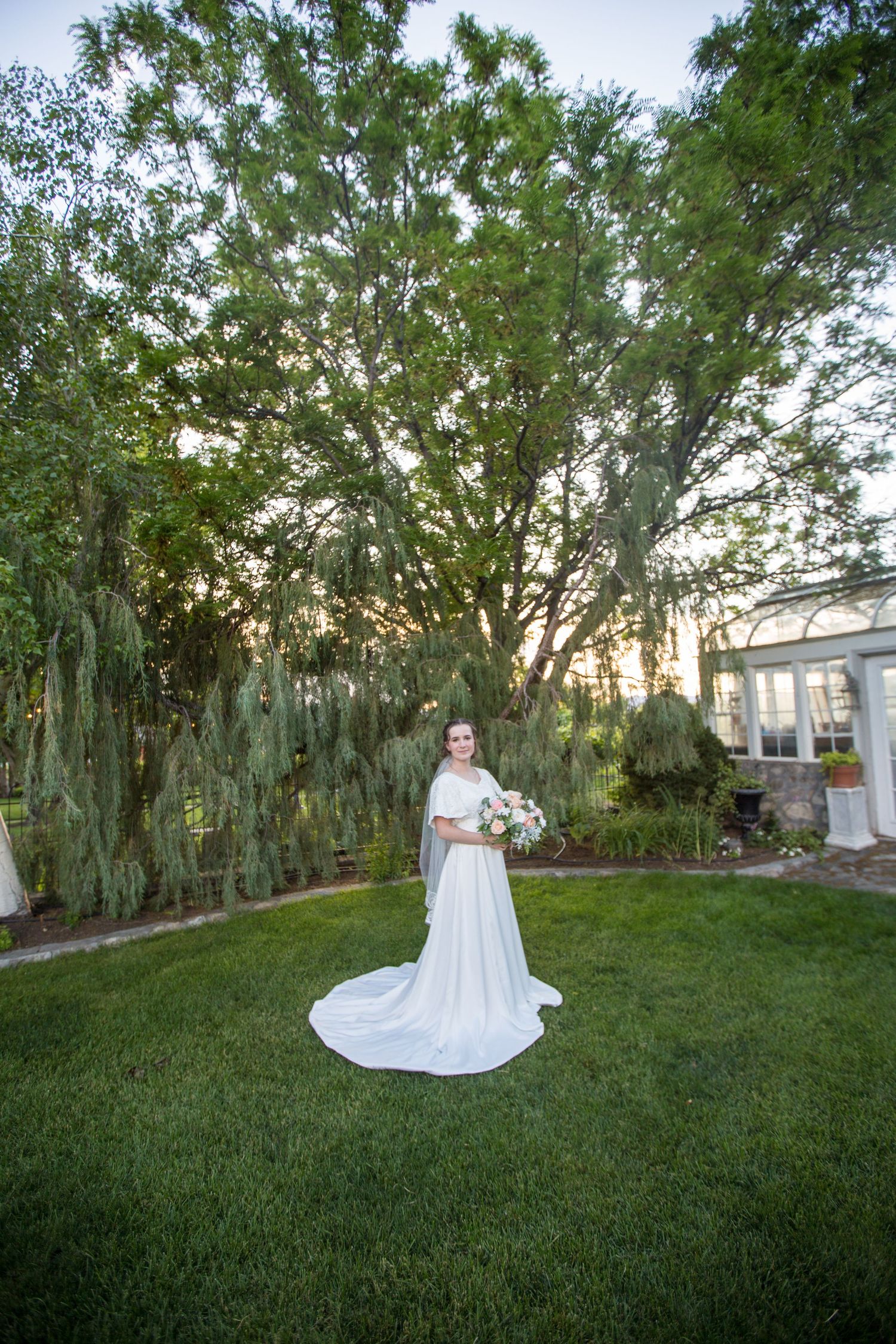 A flowing white wedding dress creates a dramatic silhouette against a grassy lawn with trees.