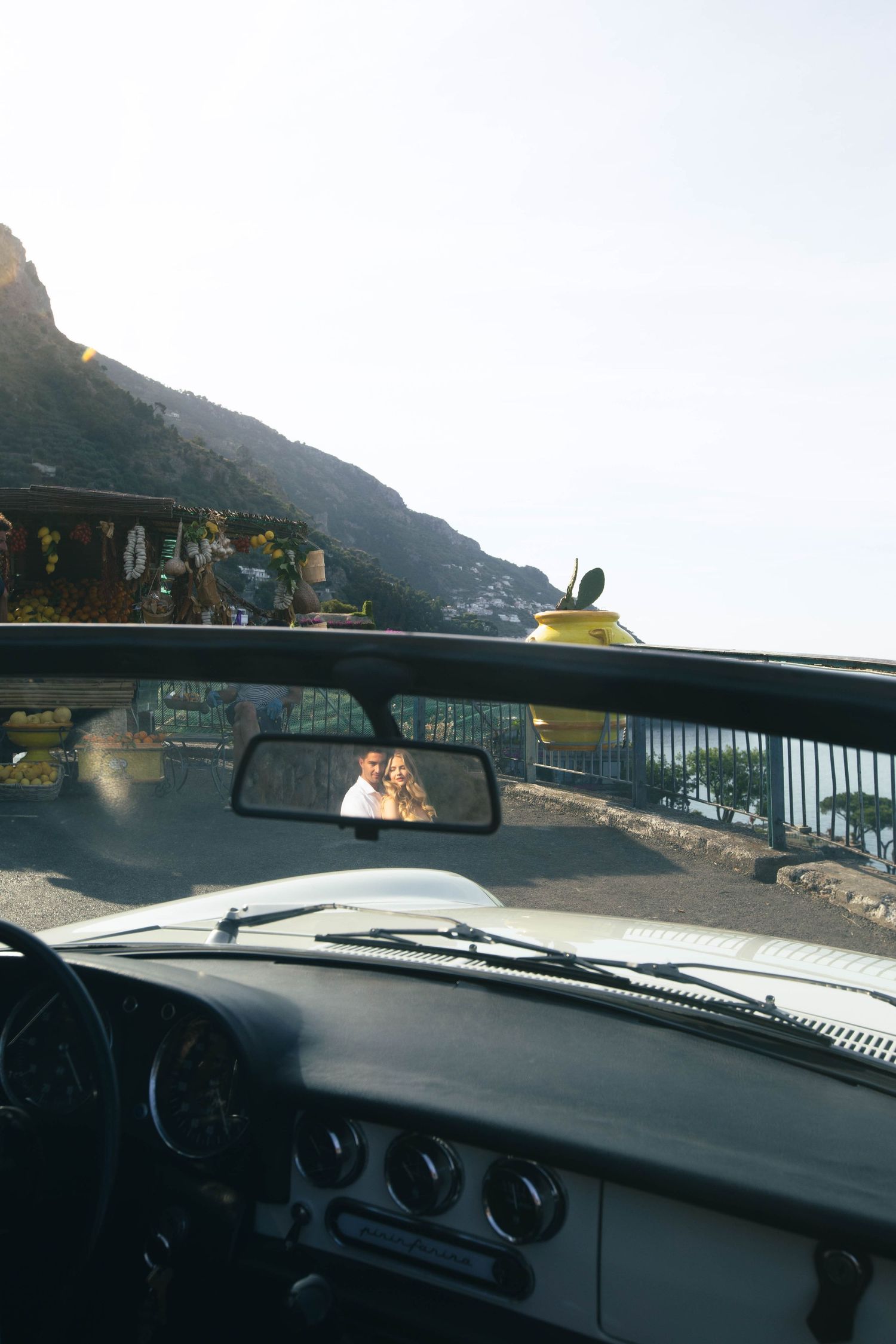 Romantic couple reflected in vintage convertible rearview mirror on the stunning Amalfi Coast road.