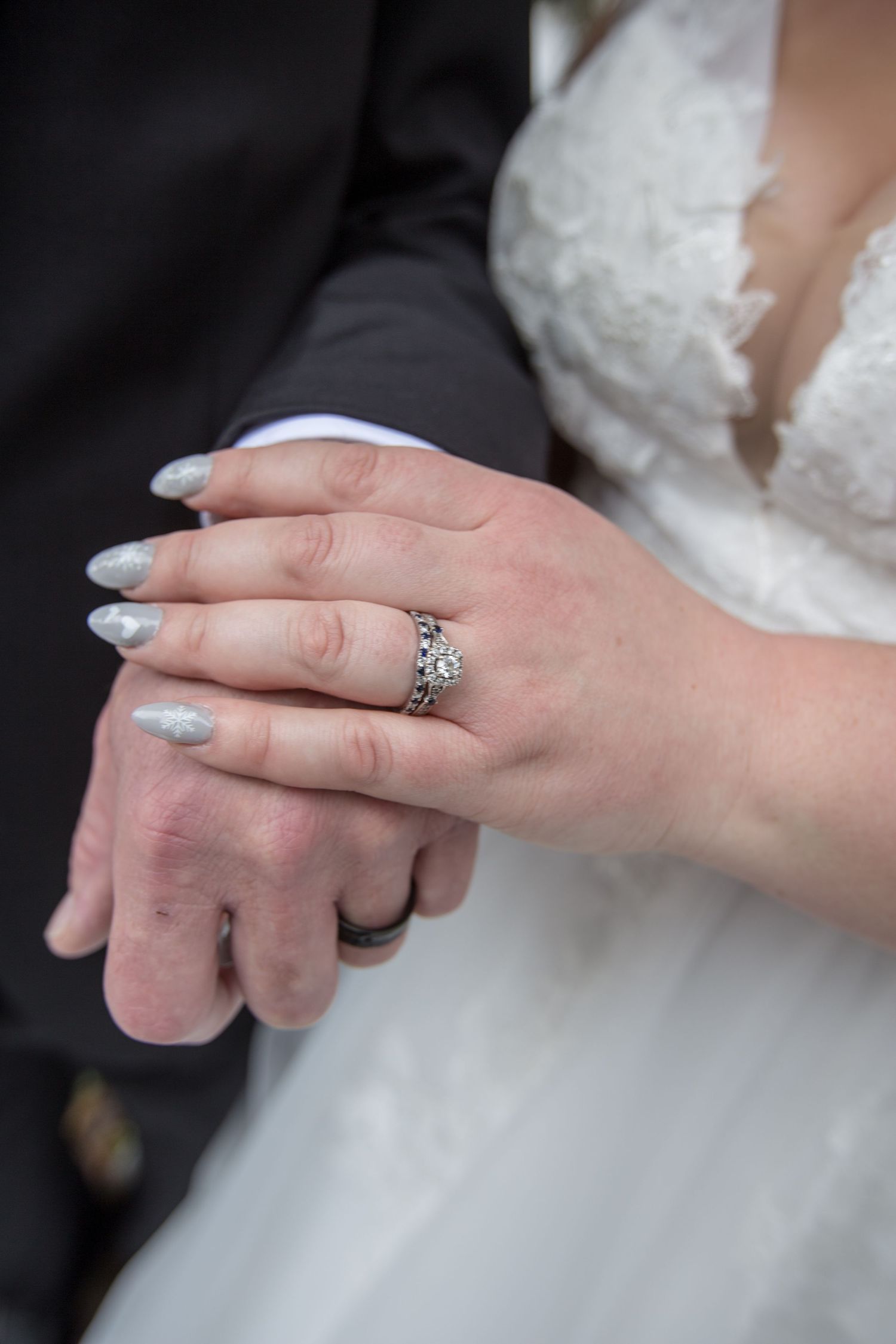 Bride and groom holding hands showing ornate diamond engagement ring and wedding bands with silver manicured nails.