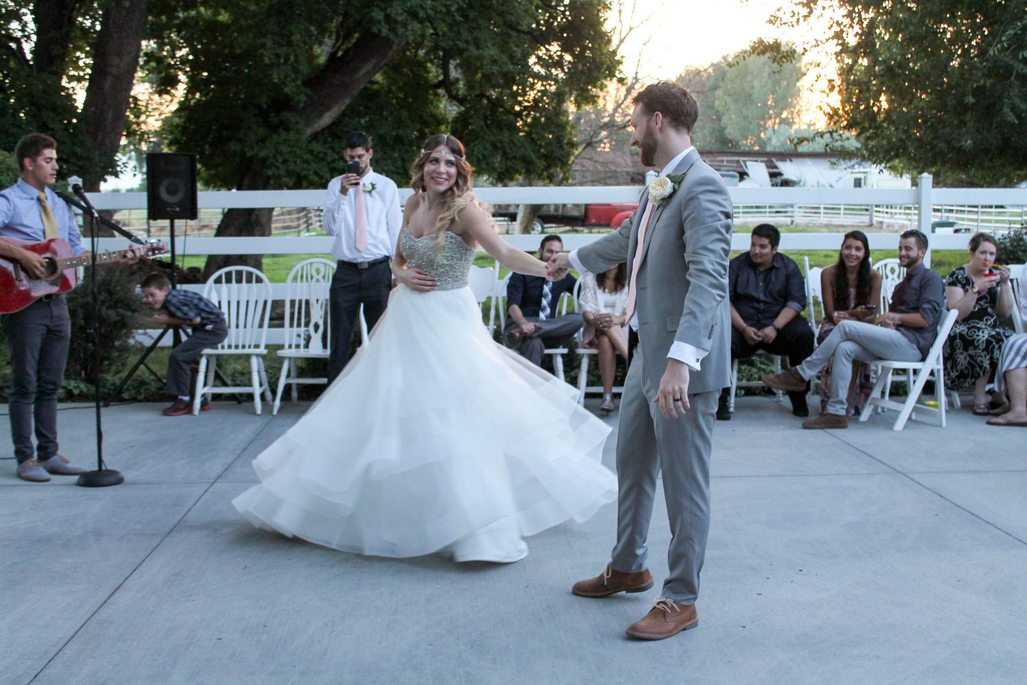 Outdoor wedding reception with guests dancing at sunset.