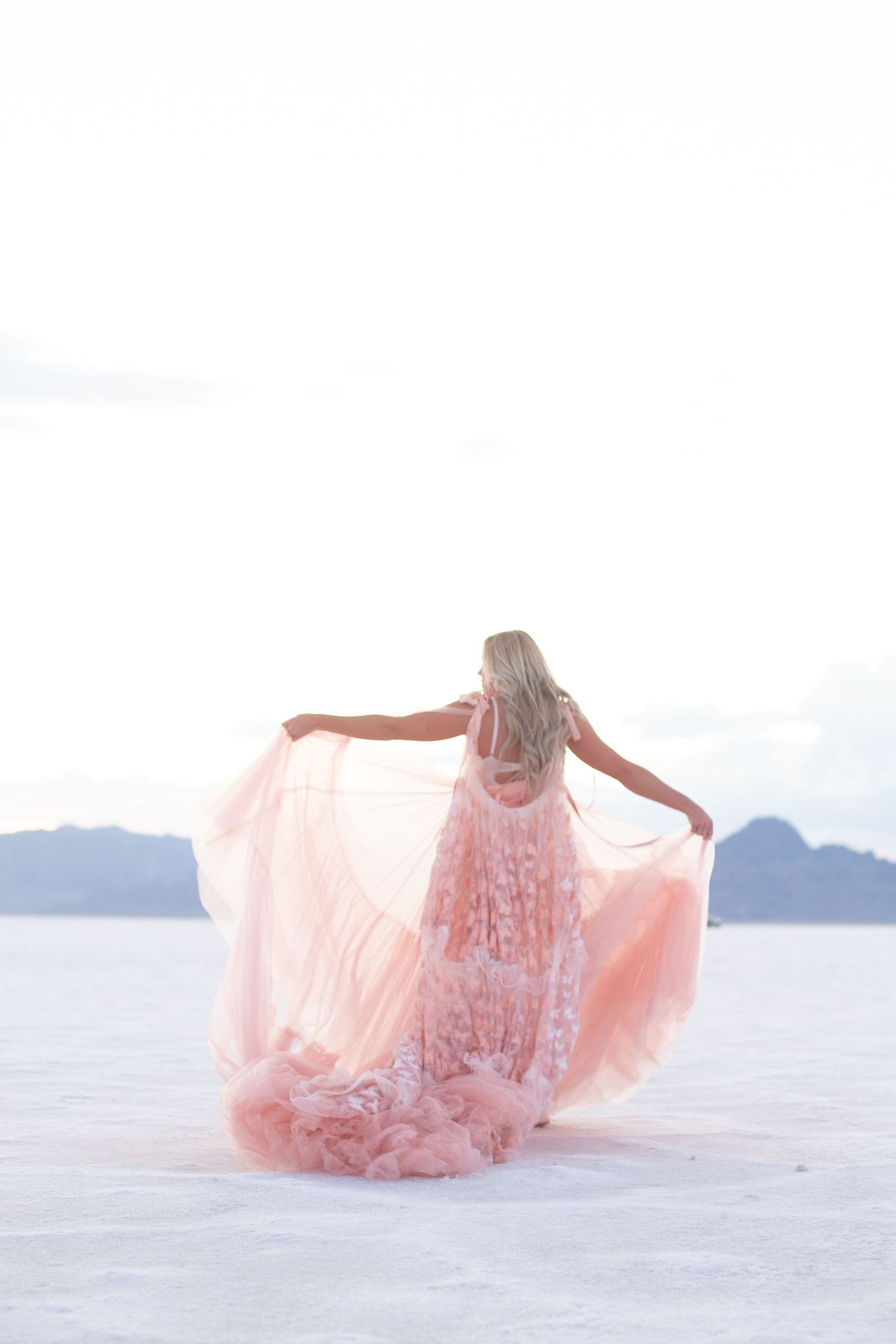 Flowing pink dress creates artistic movement against white sand and mountain landscape.
