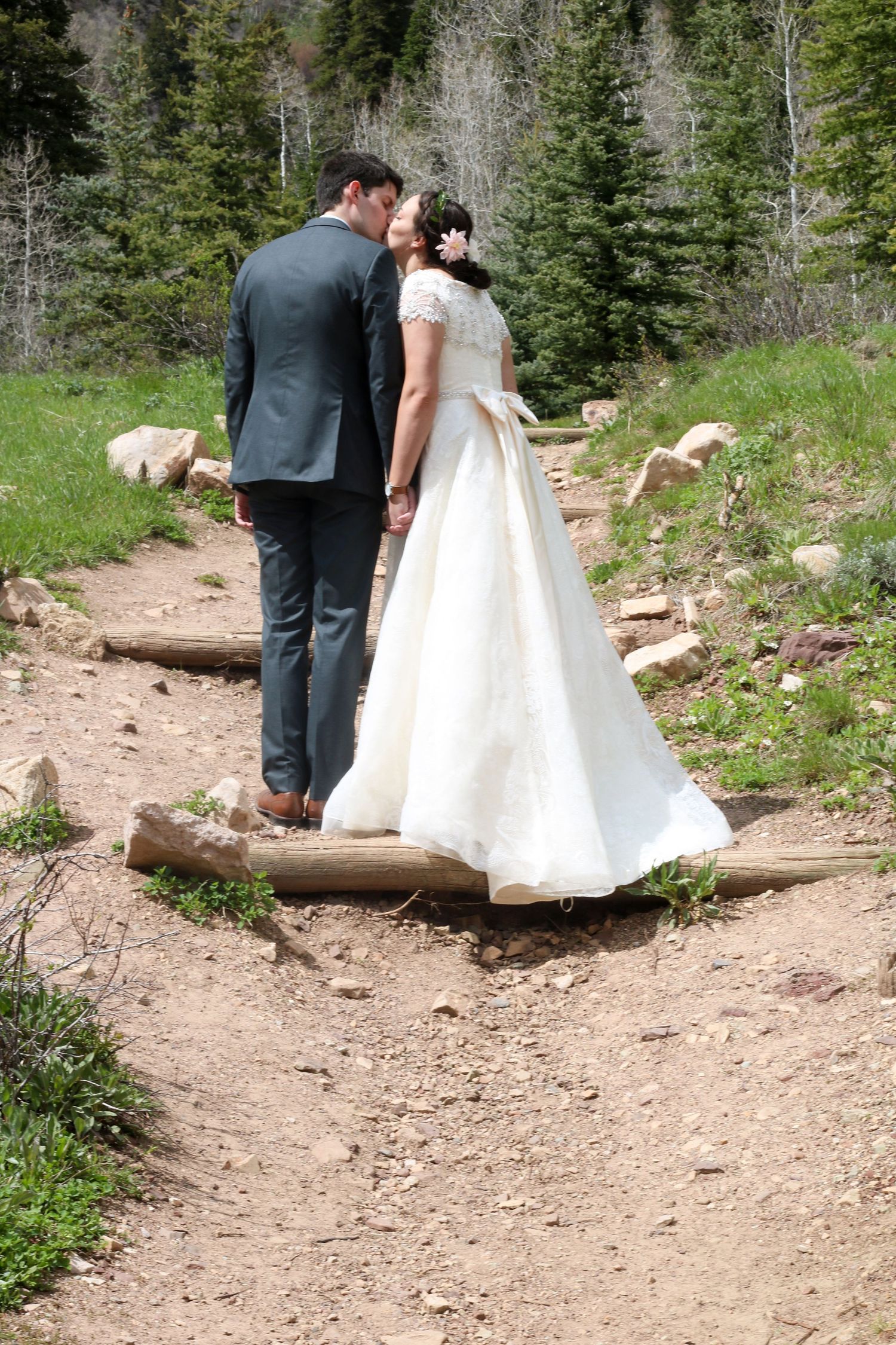 Wedding couple walks along rustic mountain trail surrounded by evergreen forest.