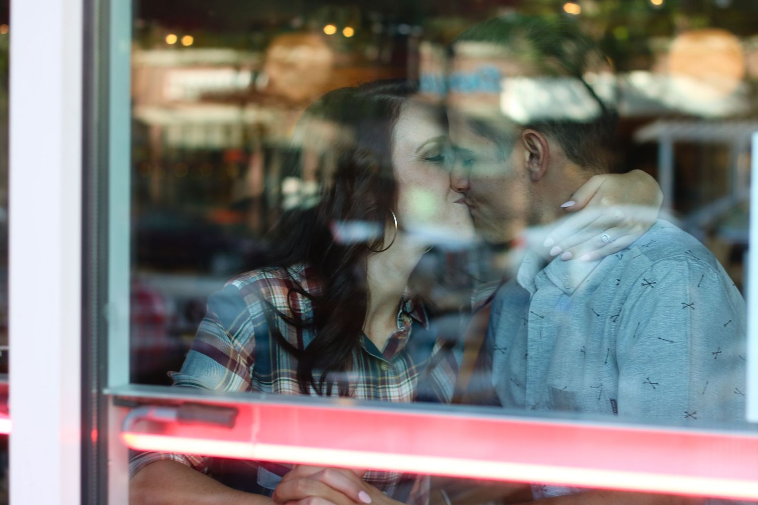 A couple is reflected in a cafe window during an intimate moment.