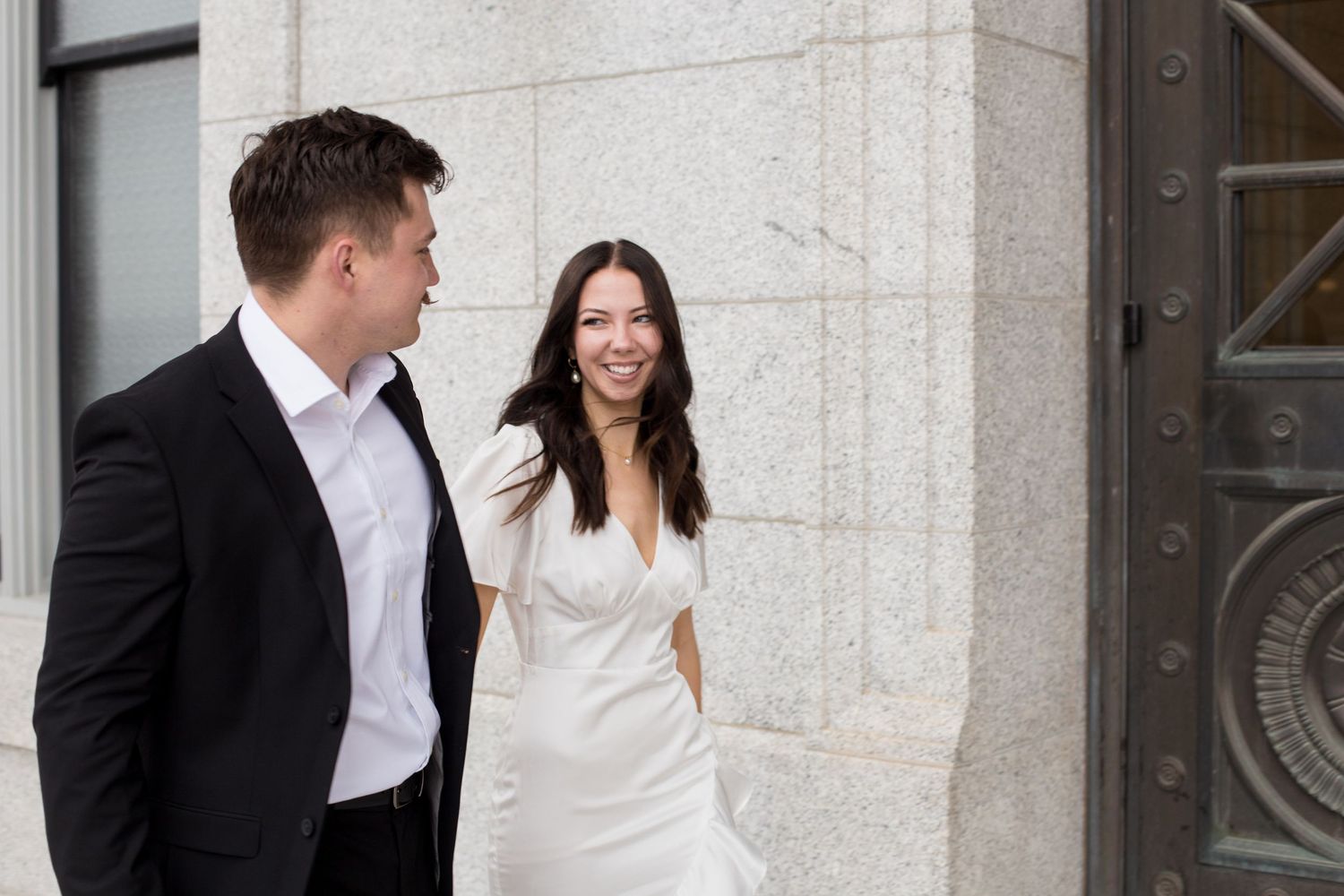 A romantic moment between a couple in formal wear standing by a grand stone building.