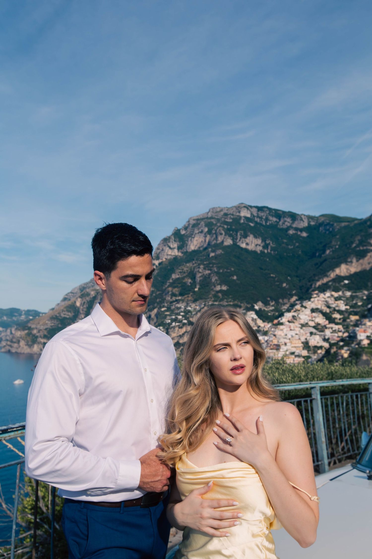 Elegant couple posing on a terrace with stunning Positano cliffside village and blue Mediterranean Sea backdrop.