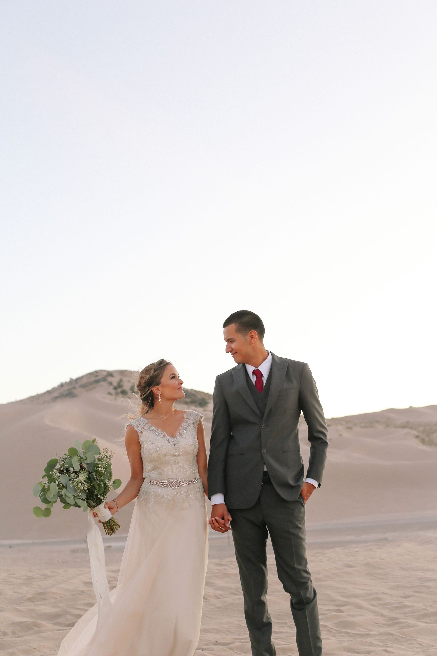 Elegant wedding portraits of couple walking through desert landscape with flowing white dress.