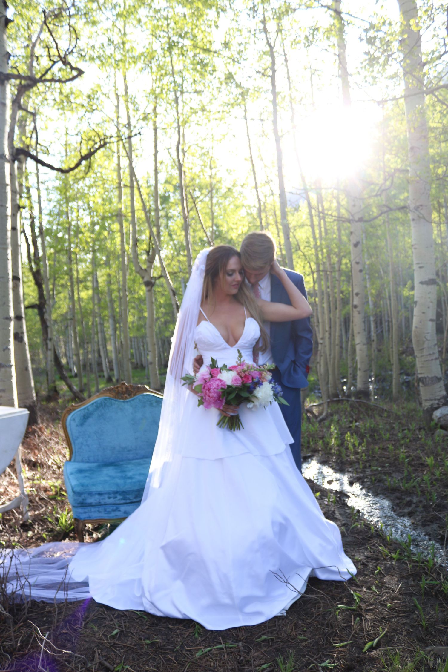 Wedding couple posing in aspen grove with sunlight filtering through trees and elegant blue furniture.