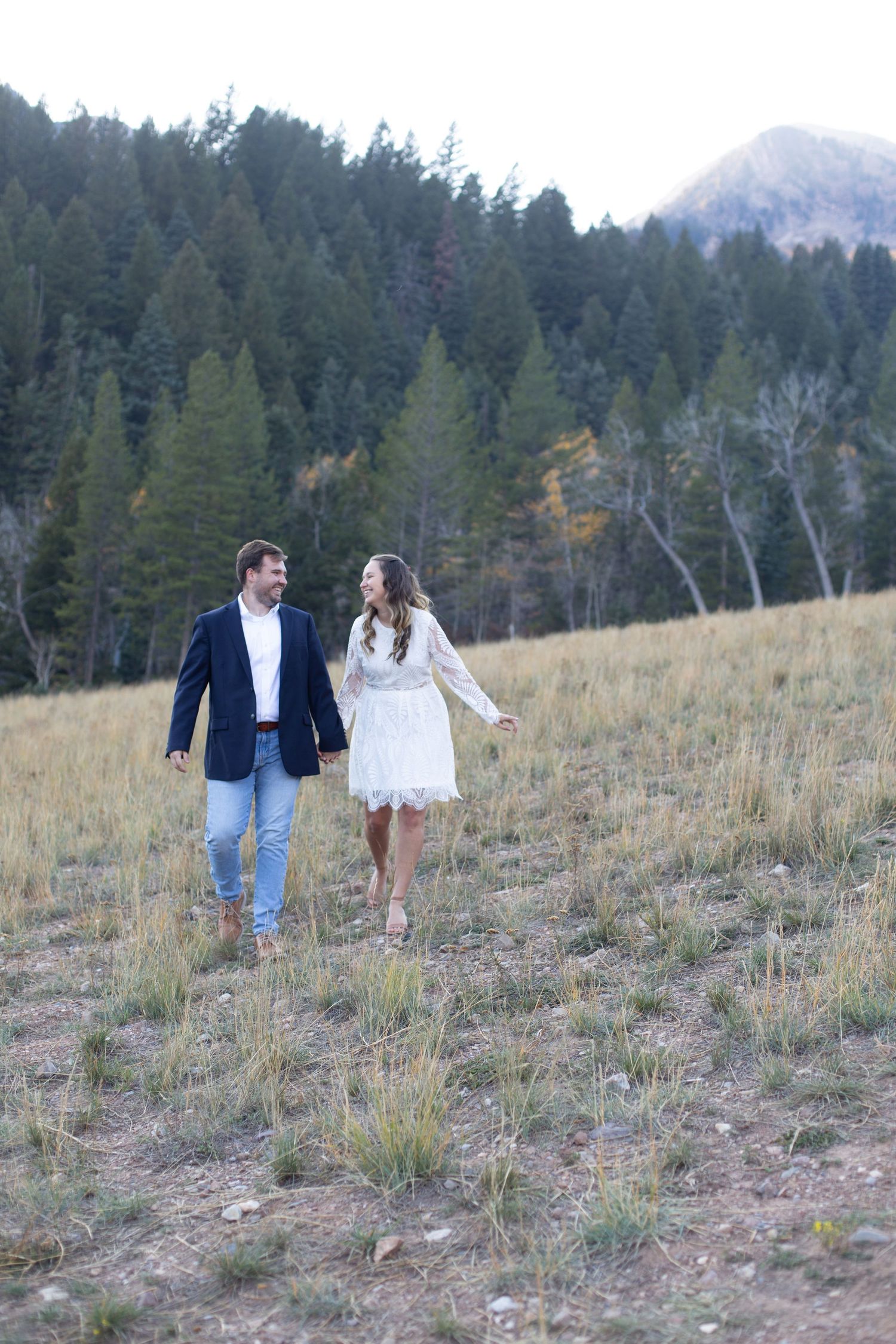 Couple walking together on a hillside with mountain forest backdrop.