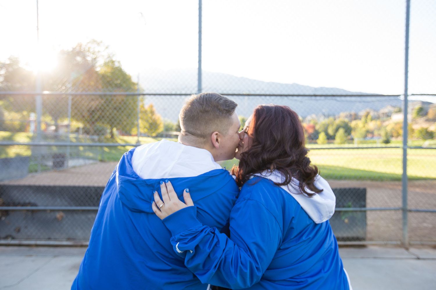 Two people in matching blue jackets share a romantic moment at sunset against a scenic backdrop.