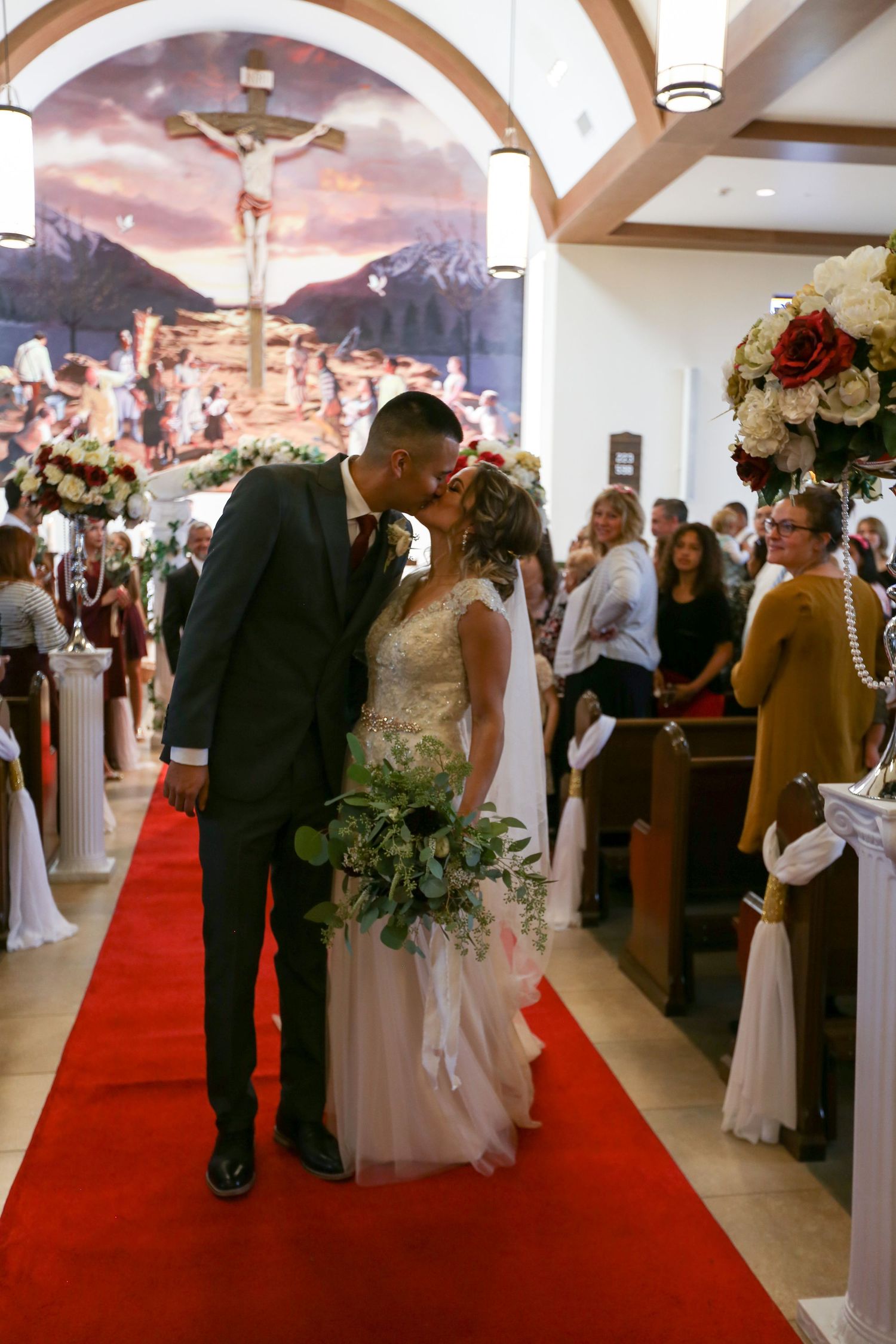 Wedding ceremony in a church with red carpet aisle and wooden arches overhead.