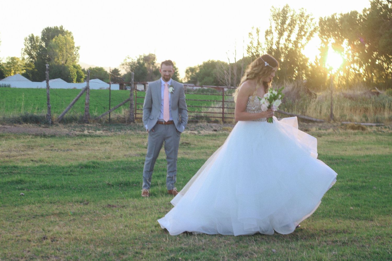 Wedding couple posing in field at sunset with flowing white dress.