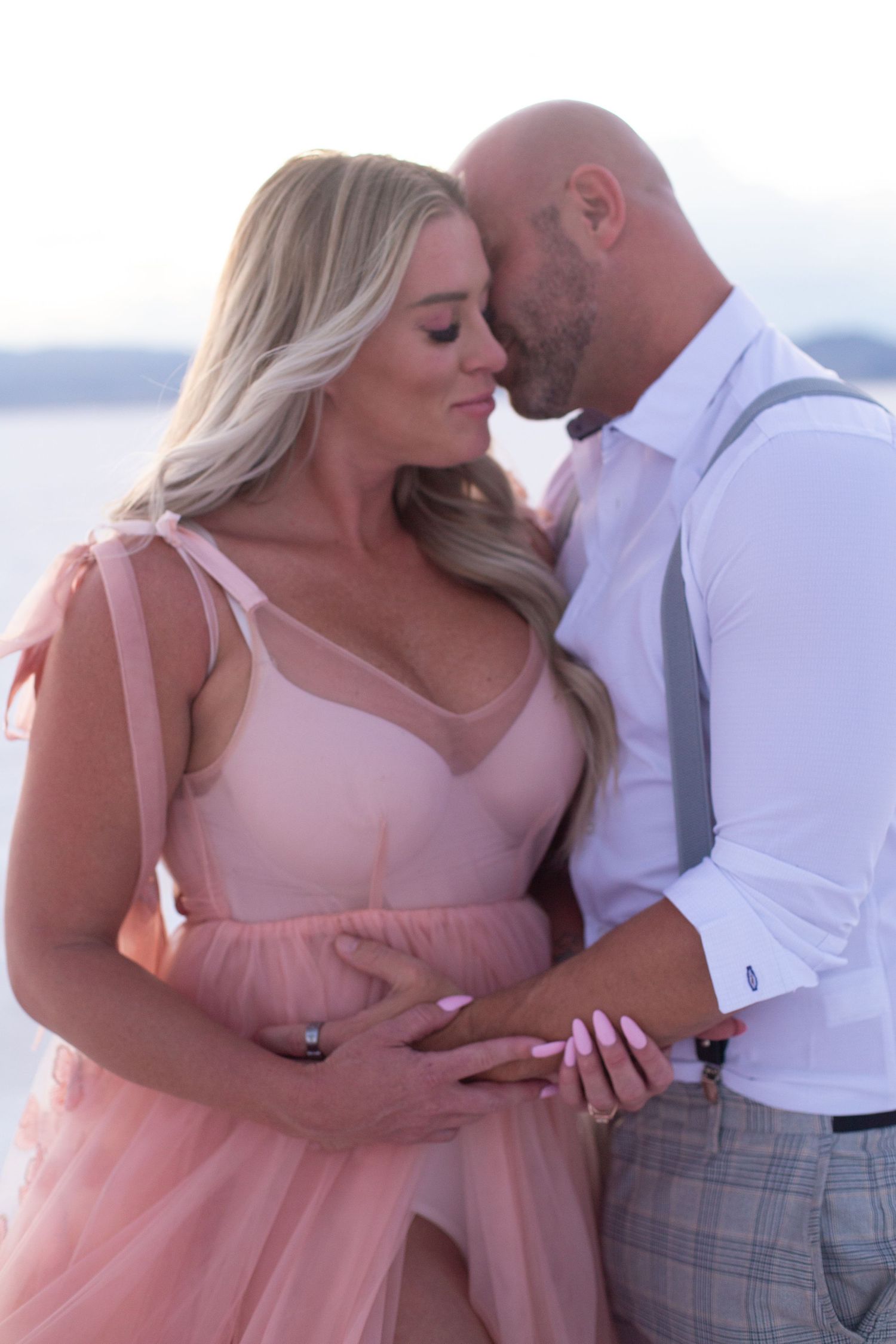 Couple shares intimate moment in pink dress and formal wear against natural backdrop.
