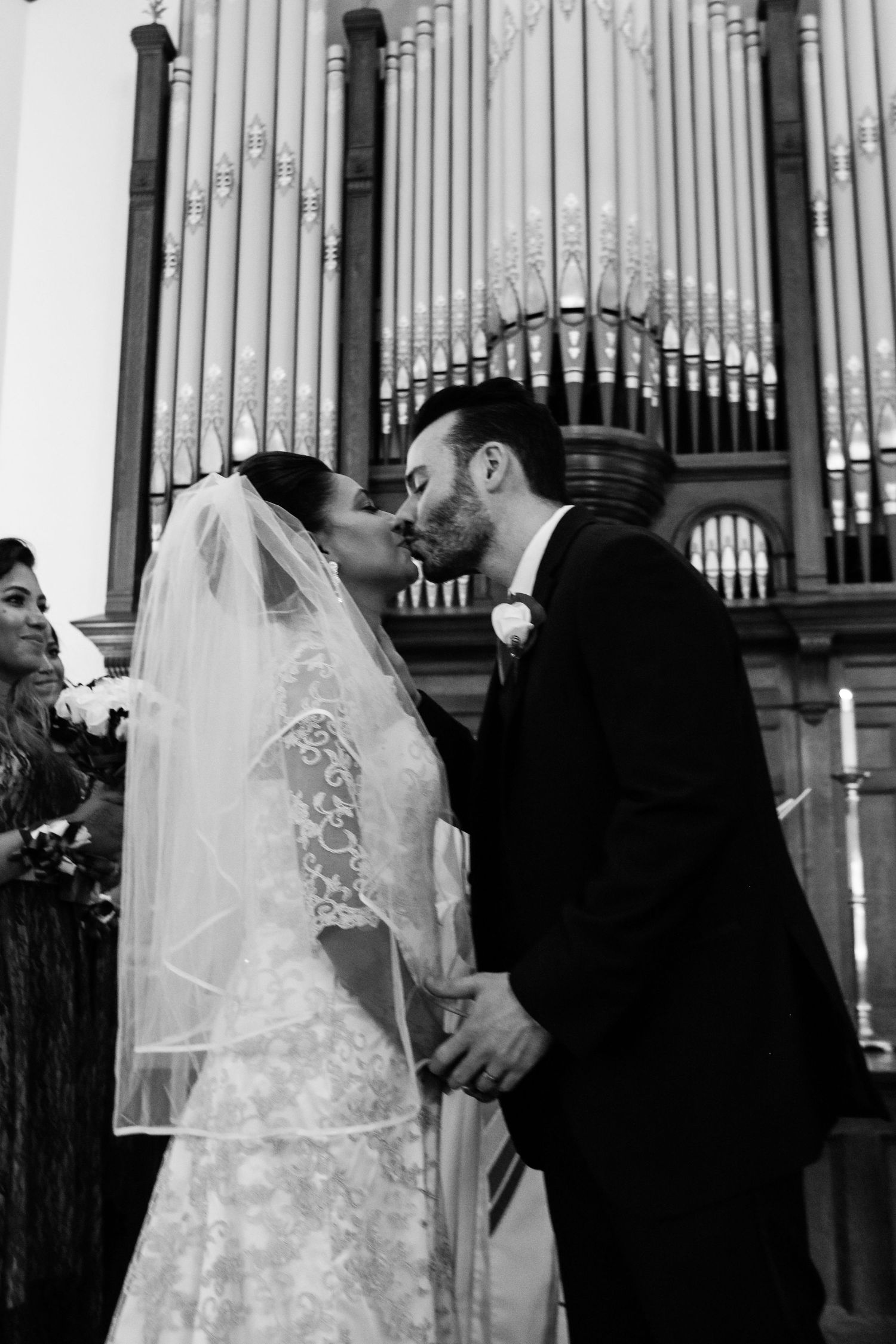 Bride and groom share first kiss at church altar with pipe organ backdrop during wedding ceremony.