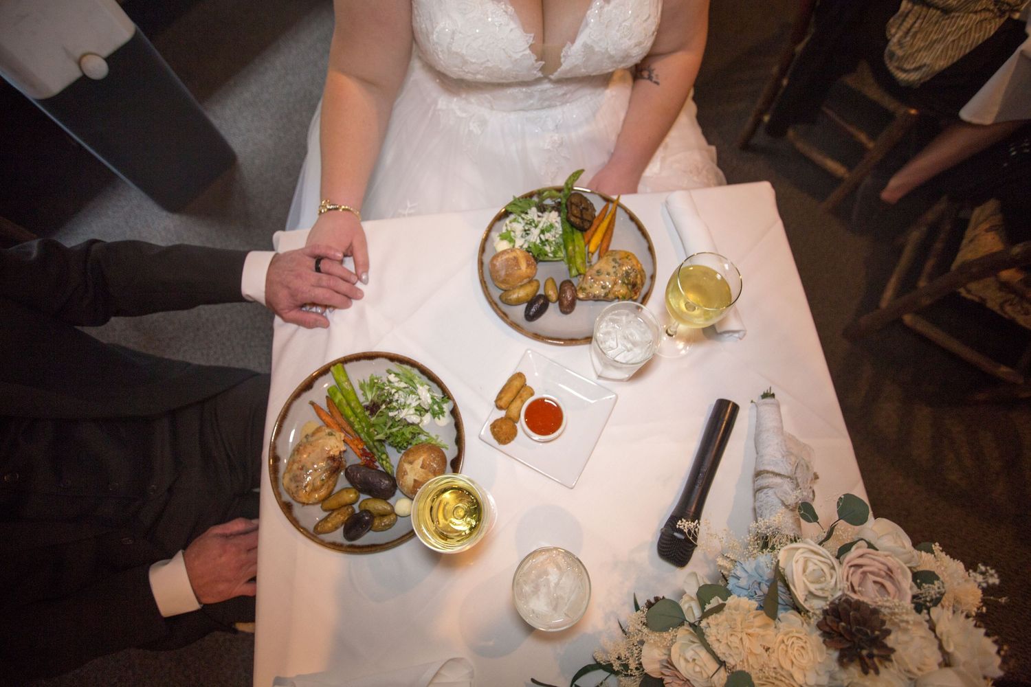 Aerial view of a bride and groom holding hands at a wedding reception table with seafood plates and white wine.