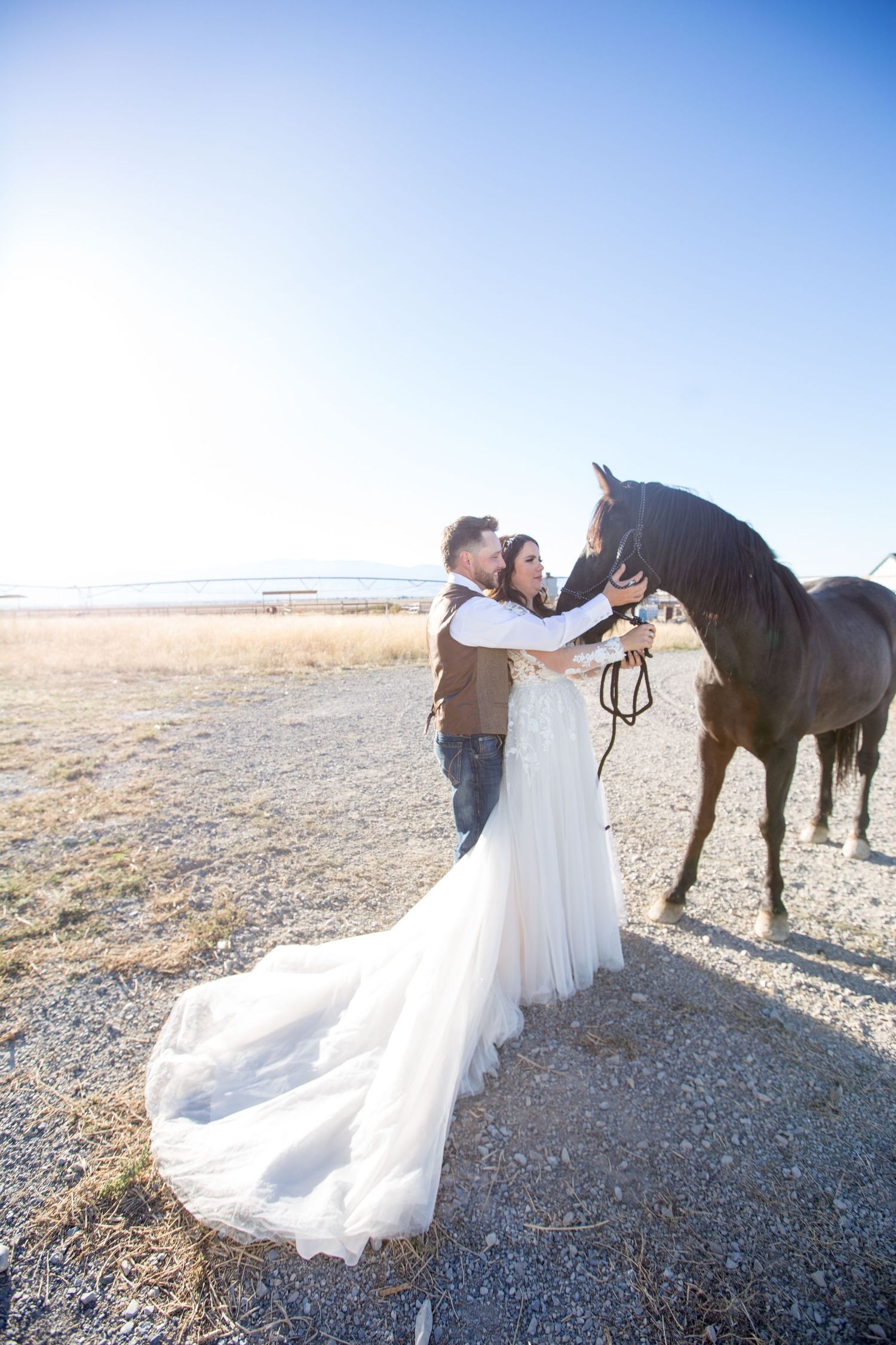 A couple in wedding attire poses with a horse in an open field.