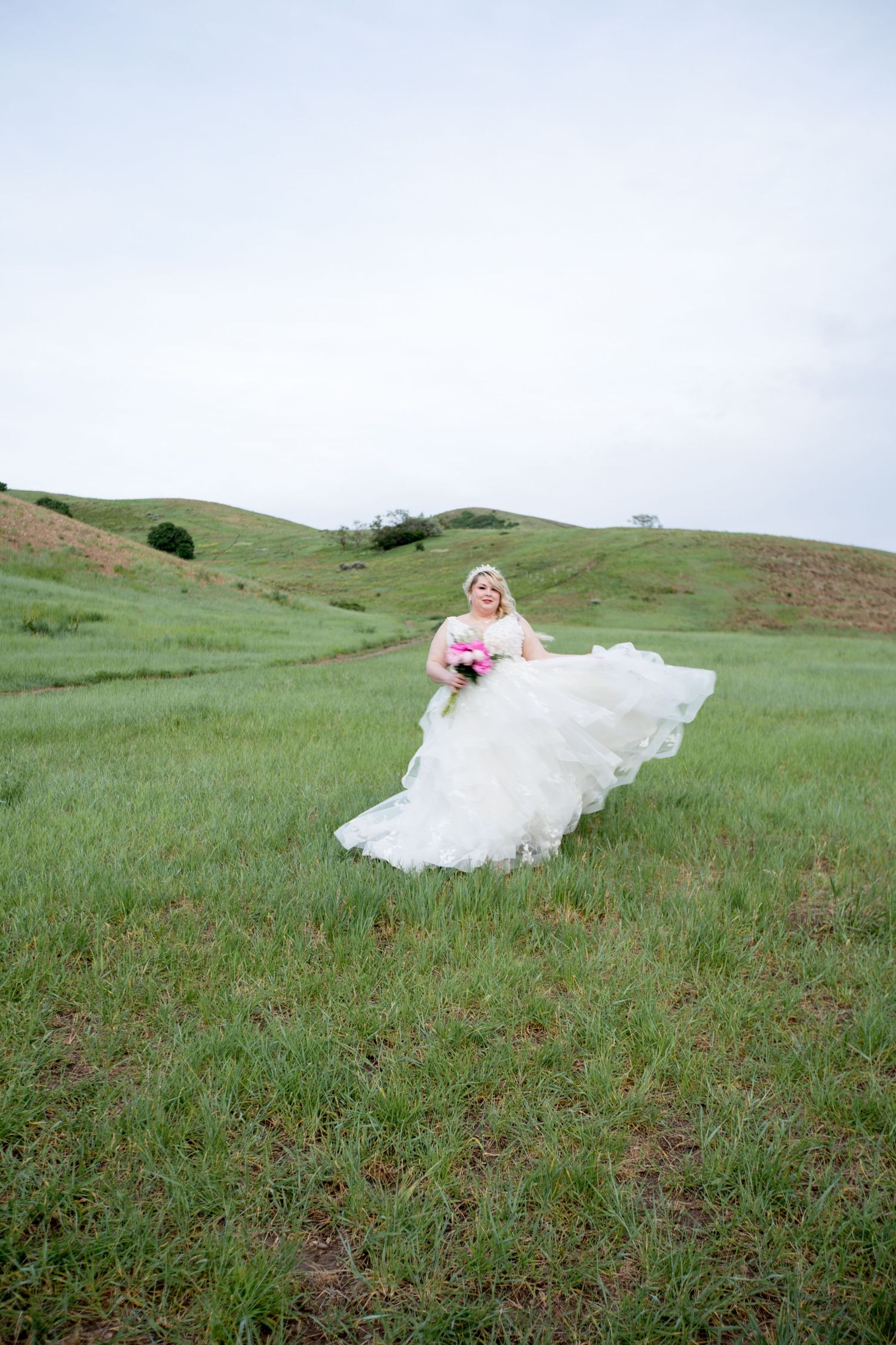 Dramatic bridal portrait with flowing dress against verdant hillside scenery.