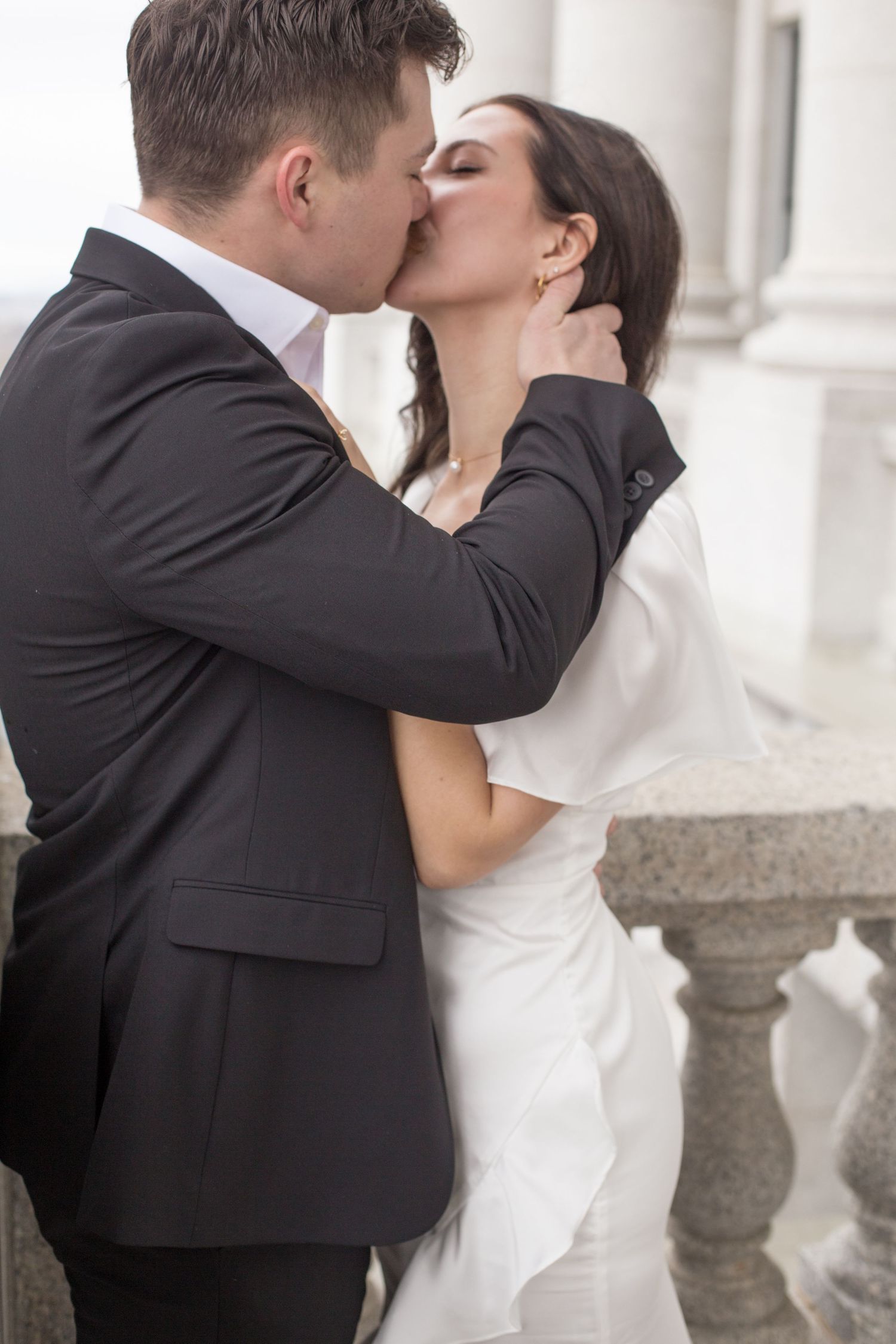 An intimate kiss between newlyweds against a backdrop of classical architecture.